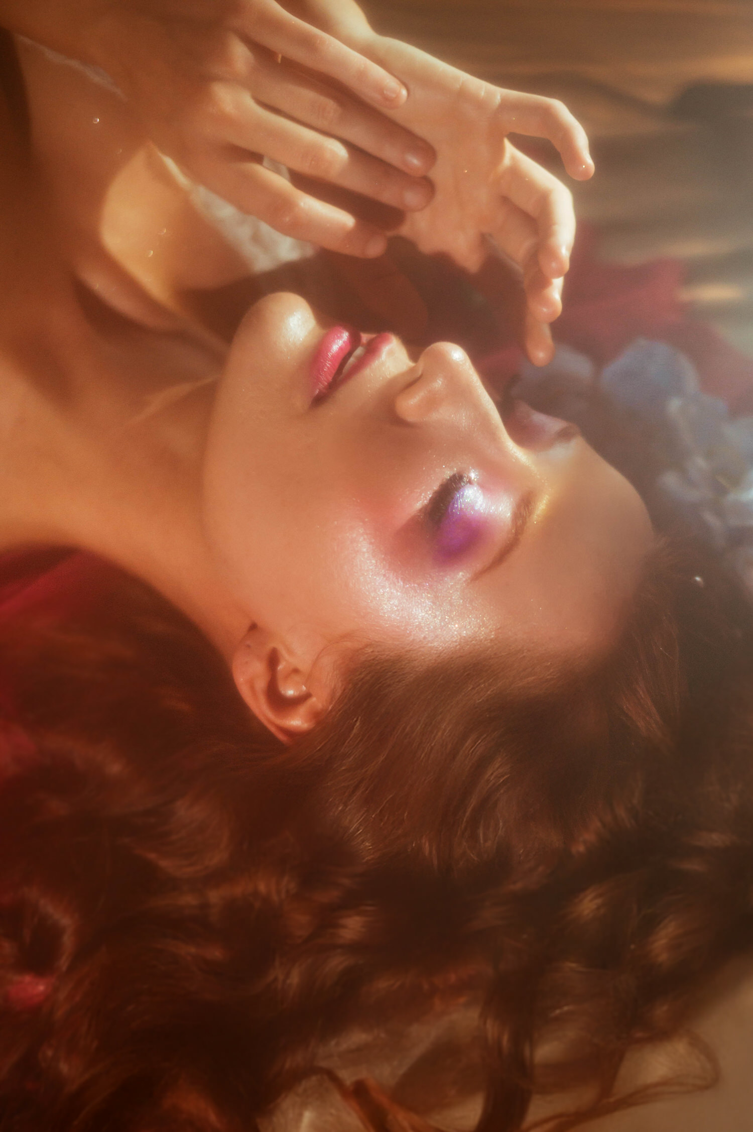 A close up portrait of a model reaching toward soft light with glossy pink makeup, captured for a fine art Midsummer Night's Dream inspired photoshoot. This dreamy photography studio image was shot near Dallas. Royal Lune Photo.