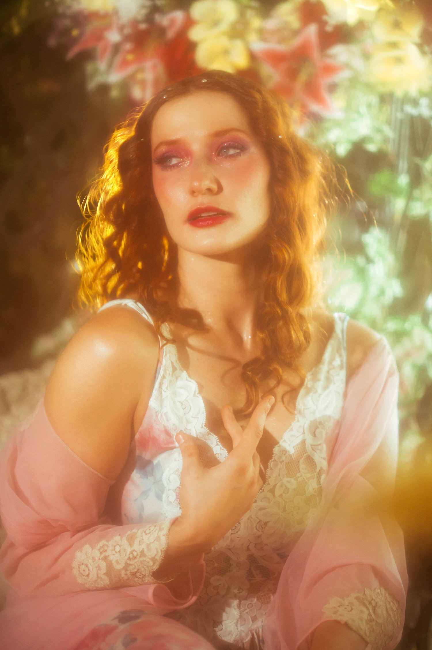 A close up portrait of a model in a lace vintage nightgown with a sheer pink wrap, surrounded by soft golden light and florals for a fine art Midsummer Night's Dream photoshoot. This dreamy photography style session took place at a Dallas area studio. Royal Lune Photo.