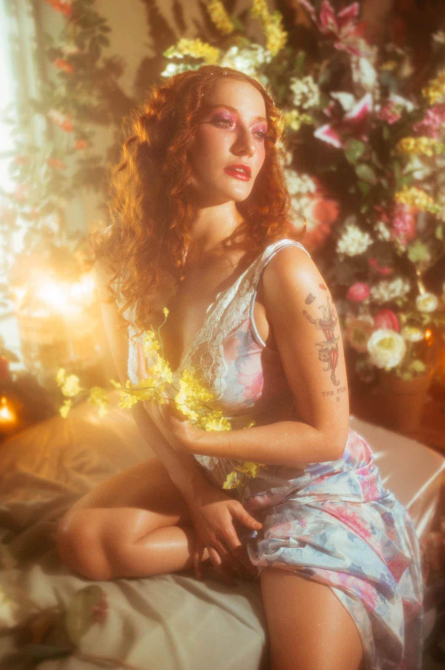 A model in a vintage floral nightgown sits among golden light and blooming flowers, showcasing the dreamy photography studio aesthetic of a Midsummer Night's Dream inspired session. This fine art portrait was created at Royal Lune Studio in the Dallas area. Royal Lune Photo.
