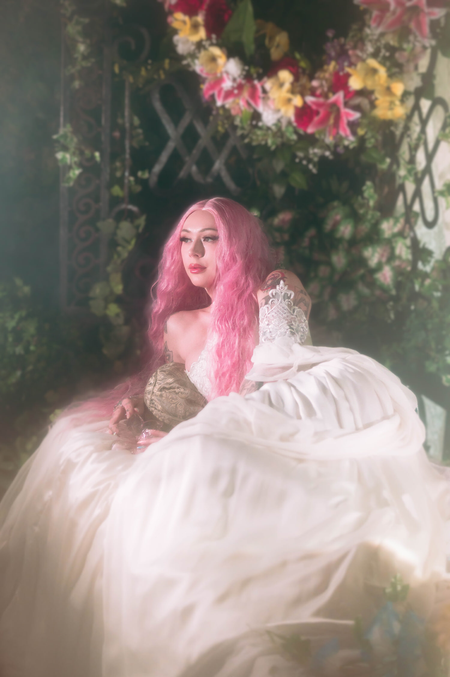 Dreamy fantasy bridal photos of bride seated beneath hanging florals, showcasing a voluminous fairytale bridal gown with soft diffused lighting.