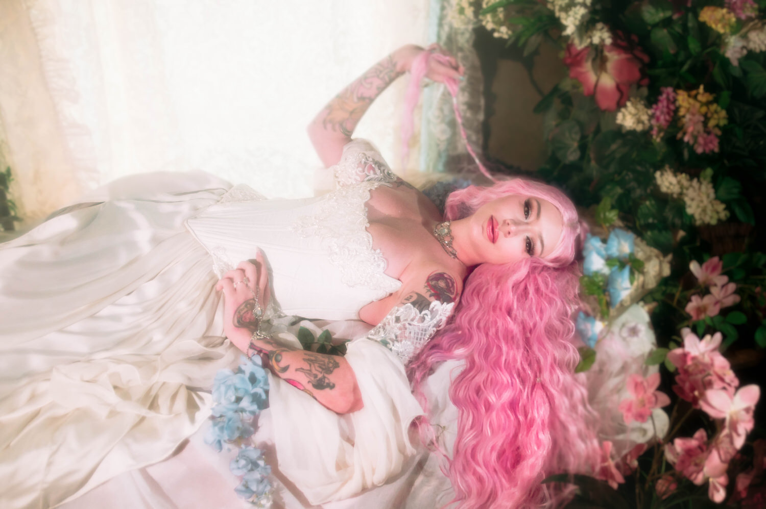 Overhead bridal portrait of bride reclining in a fantasy bridal gown with cascading pink hair and soft pastel florals.