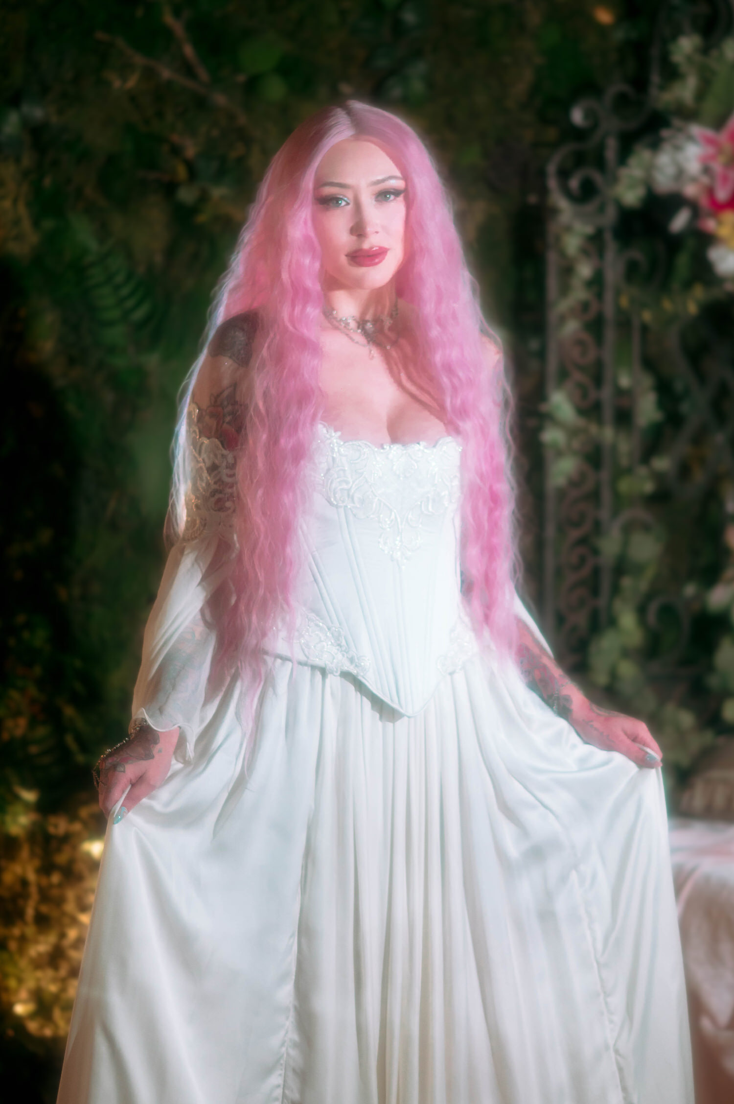 Portrait of bride in a structured white corset fantasy bridal gown with flowing sleeves, standing in a romantic garden-inspired fantasy wedding photography set.