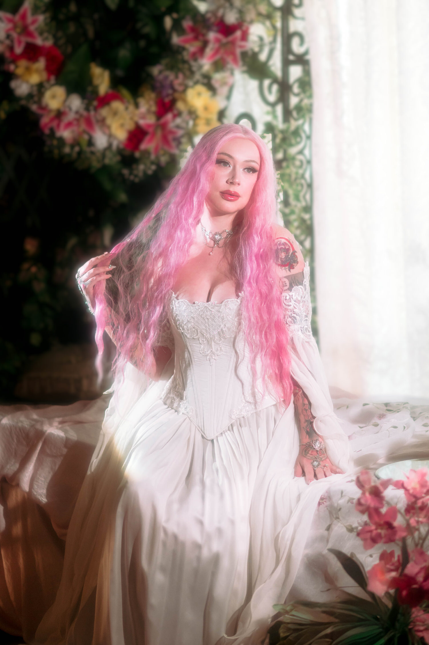 Bride seated among florals and greenery wearing a fairytale bridal gown with lace corset detailing, styled in a soft, ethereal renaissance fair wedding photography scene.