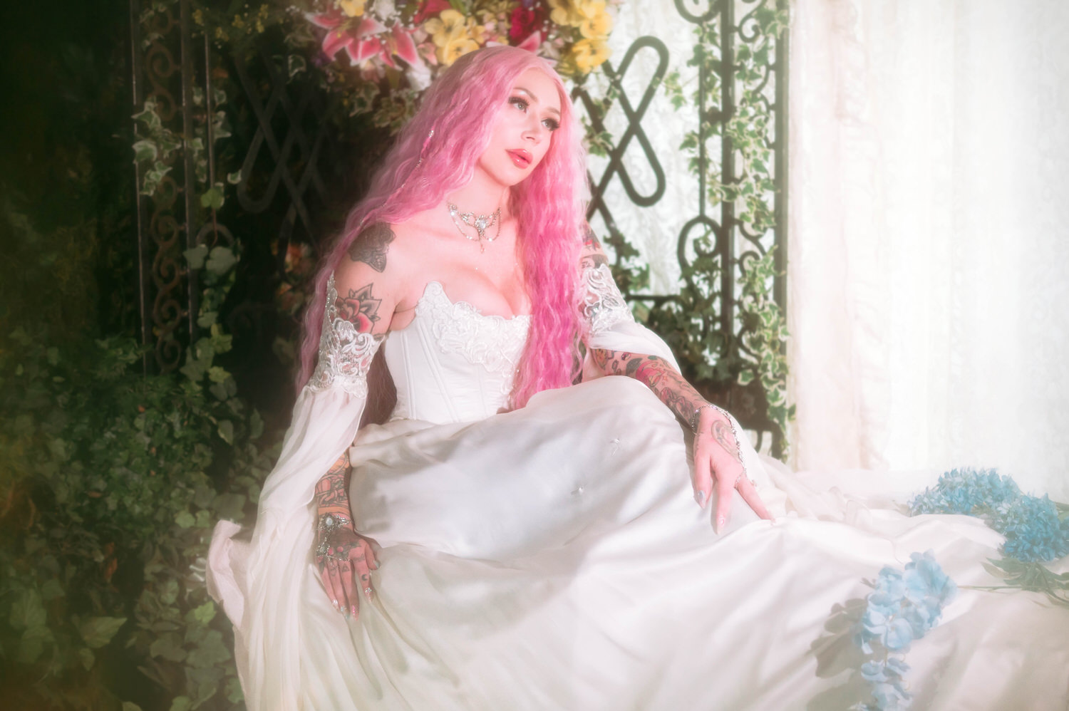 Bride seated before ornate ironwork gate and florals in a voluminous fairytale bridal gown, styled for renaissance fair wedding photography.