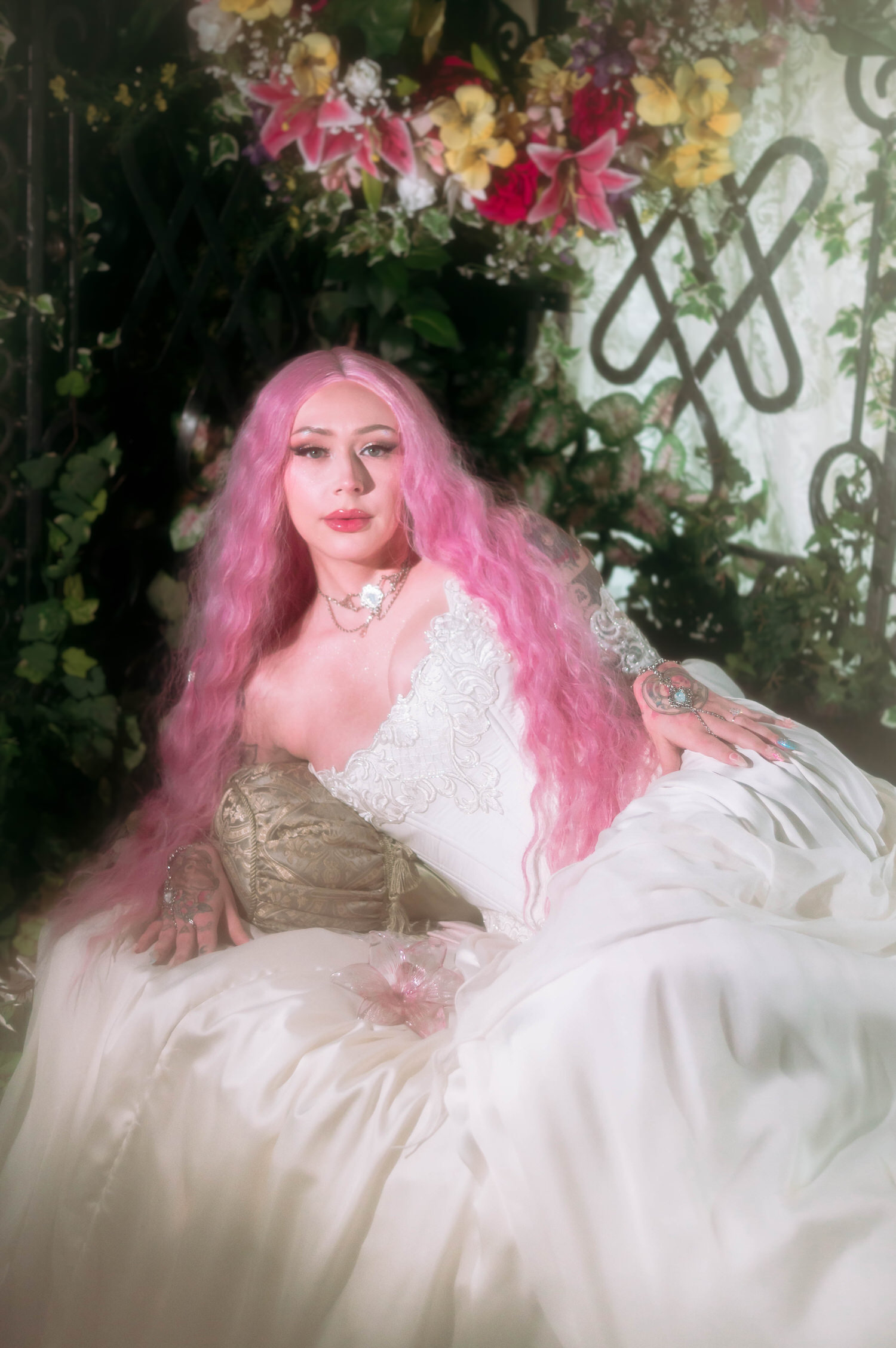 Romantic bridal portrait featuring a structured fantasy bridal gown with lace appliqué sleeves, pink hair glowing in soft window light.