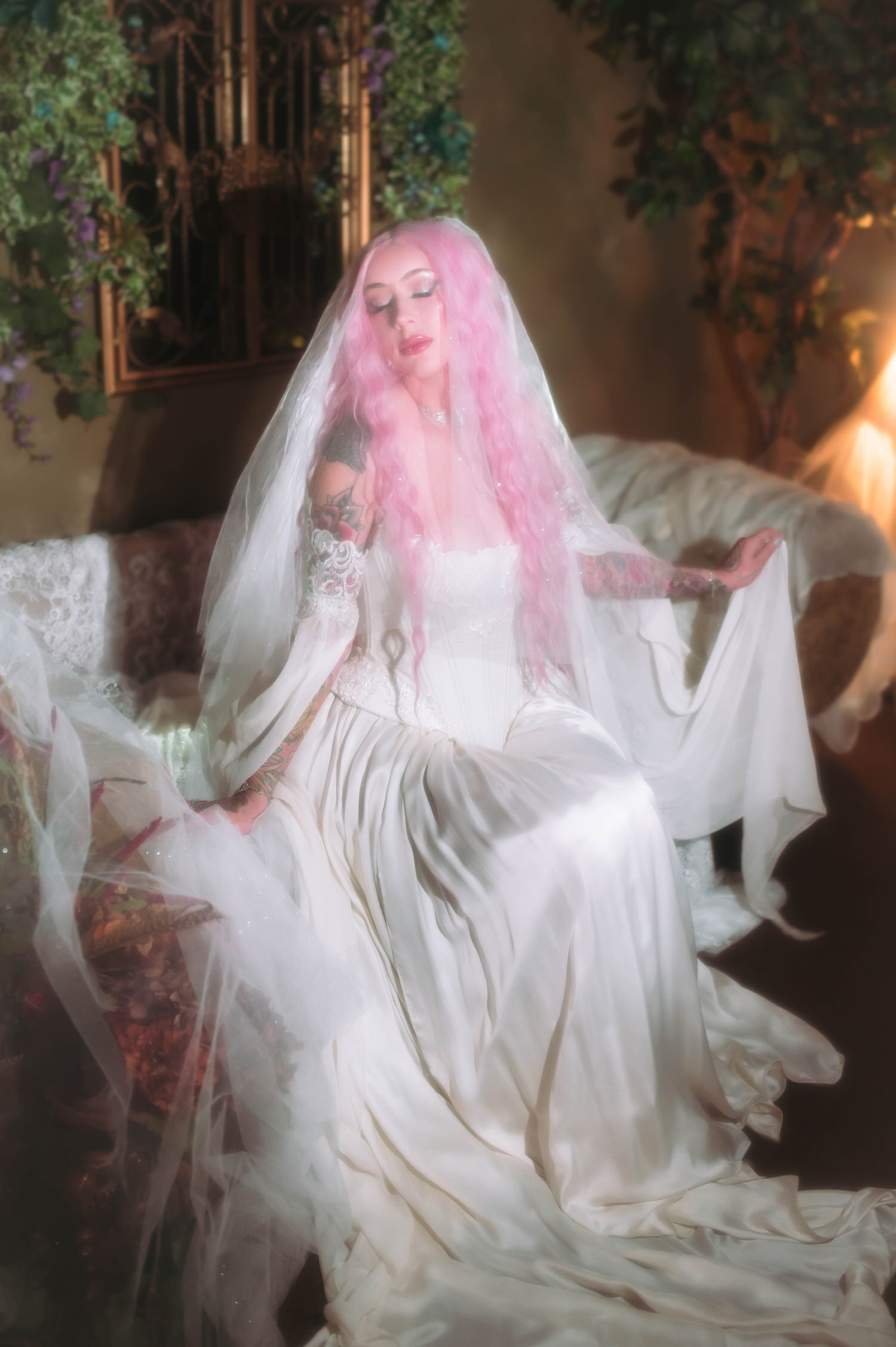Bridal portrait featuring a fairytale bridal gown with long chiffon sleeves and veil, posed on antique sofa surrounded by ivy and warm golden light.