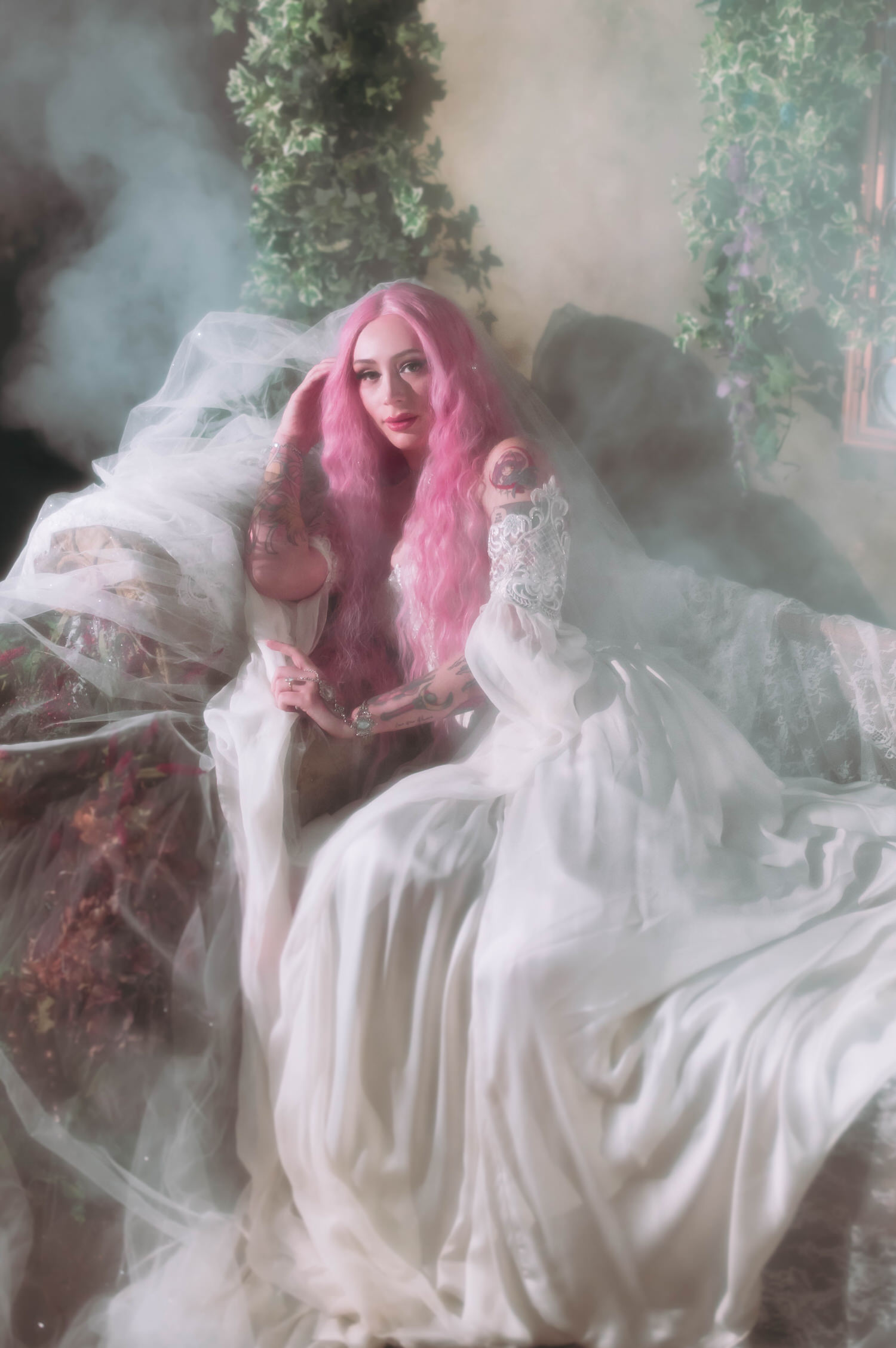 Fantasy wedding photography of bride reclining on vintage couch in a flowing firefly path bridal gown, layered tulle and soft fog creating a romantic fairytale atmosphere.
