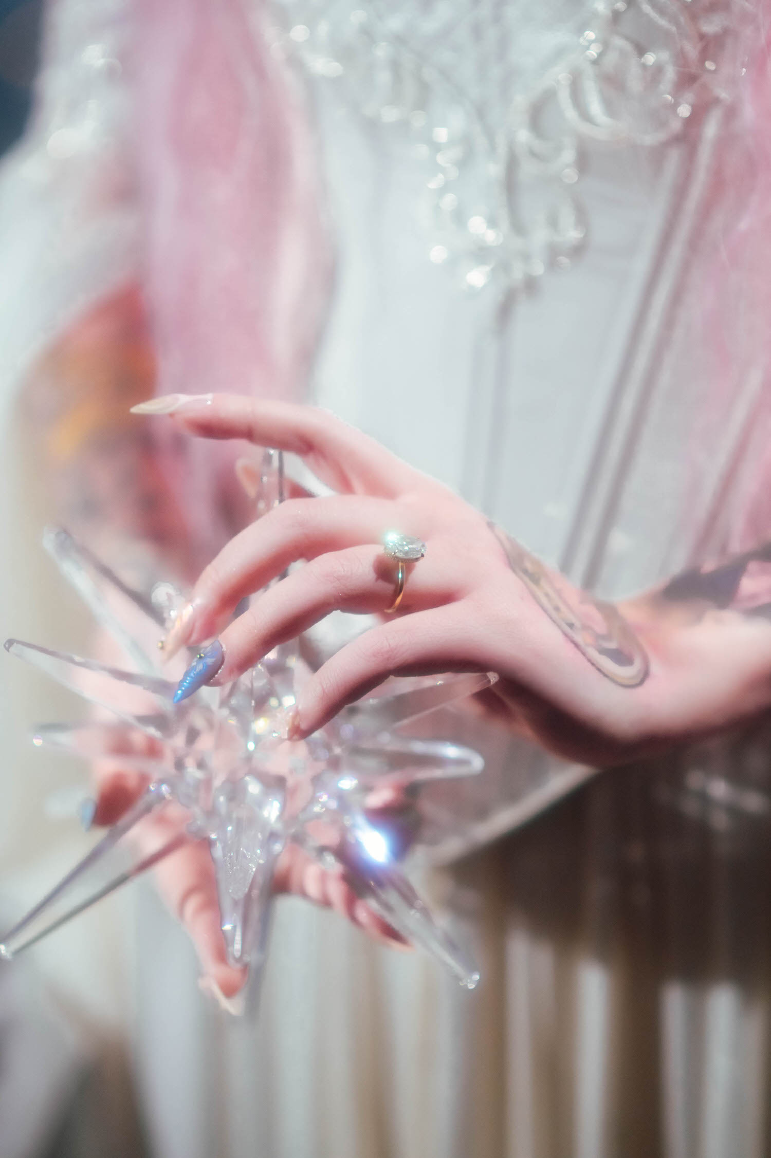 Macro detail of bride’s hand with engagement ring holding a crystal star prop, styled for fantasy wedding photography with soft pastel lighting.
