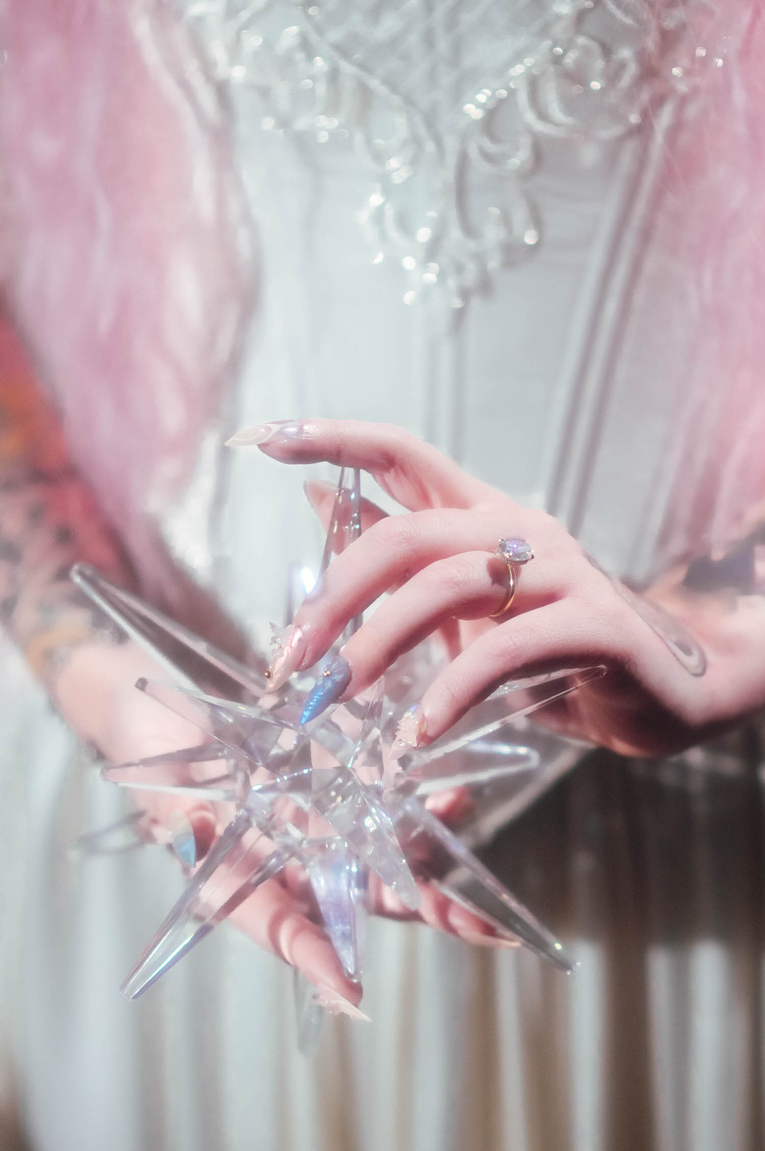Close-up of manicured hands and engagement ring gripping a clear star ornament, highlighting delicate lace corset details in a fairytale bridal gown.