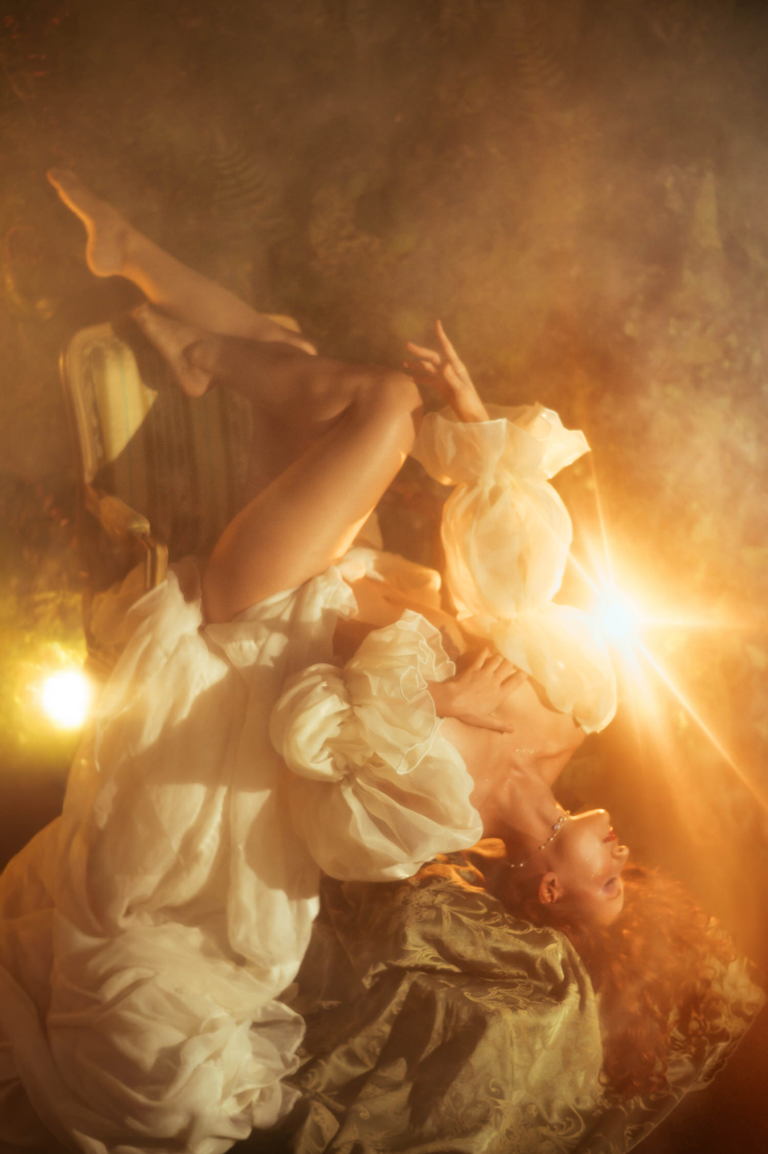 A fine art nude portrait on an antique chaise lounge with sheer ivory fabric and dramatic golden backlight, reflecting the dreamy photography style of a Midsummer Night's Dream inspired session. This artistic image was created at a Dallas area studio. Royal Lune Photo.