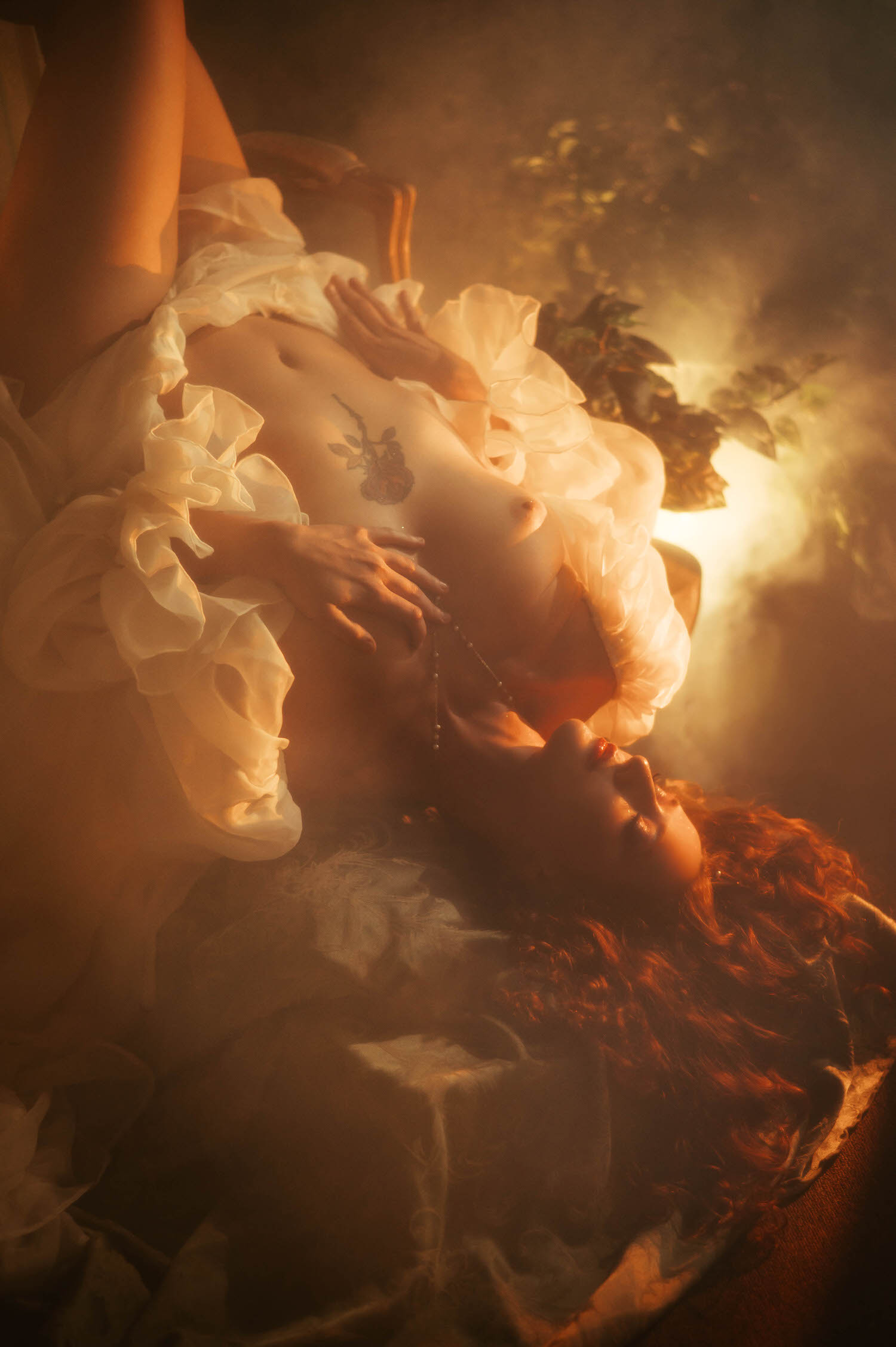 A close up fine art nude portrait with sheer ivory fabric and a delicate pearl necklace, captured in warm golden light reflecting the dreamy photography style of a Midsummer Night's Dream inspired session. This artistic image was created at a Dallas area studio. Royal Lune Photo.