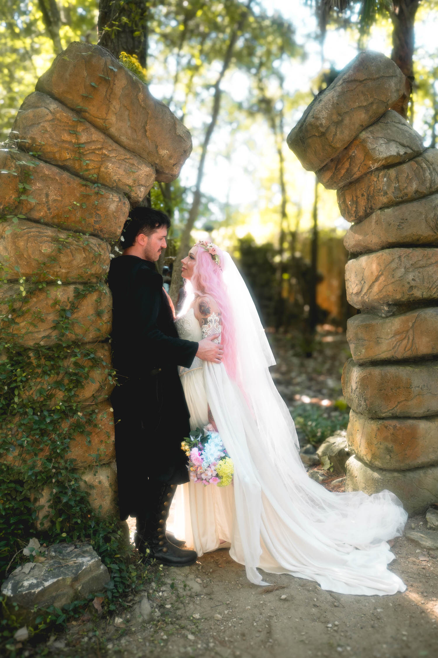 The groom embraces the bride from behind within the stone archway, her bouquet and flowing veil adding a romantic touch to the wooded scene. This kind of fairytale framing is a signature look for a fantasy wedding photographer. Royal Lune Photo.