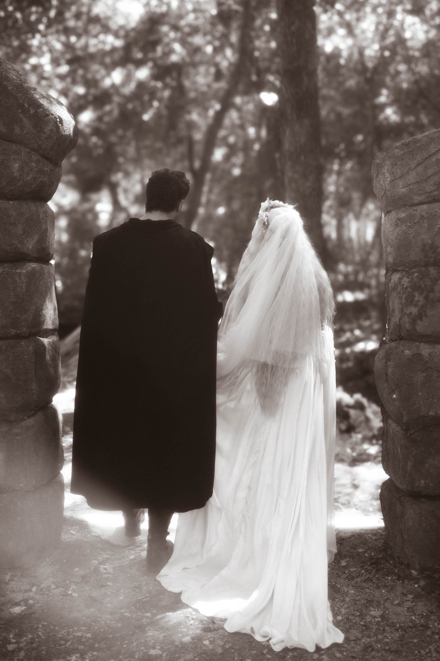 In this black and white portrait, the bride and groom walk hand in hand through the stone archway and into the trees beyond. Quiet, storybook moments like this round out the visual narrative of a Texas Renaissance Festival wedding. Royal Lune Photo.