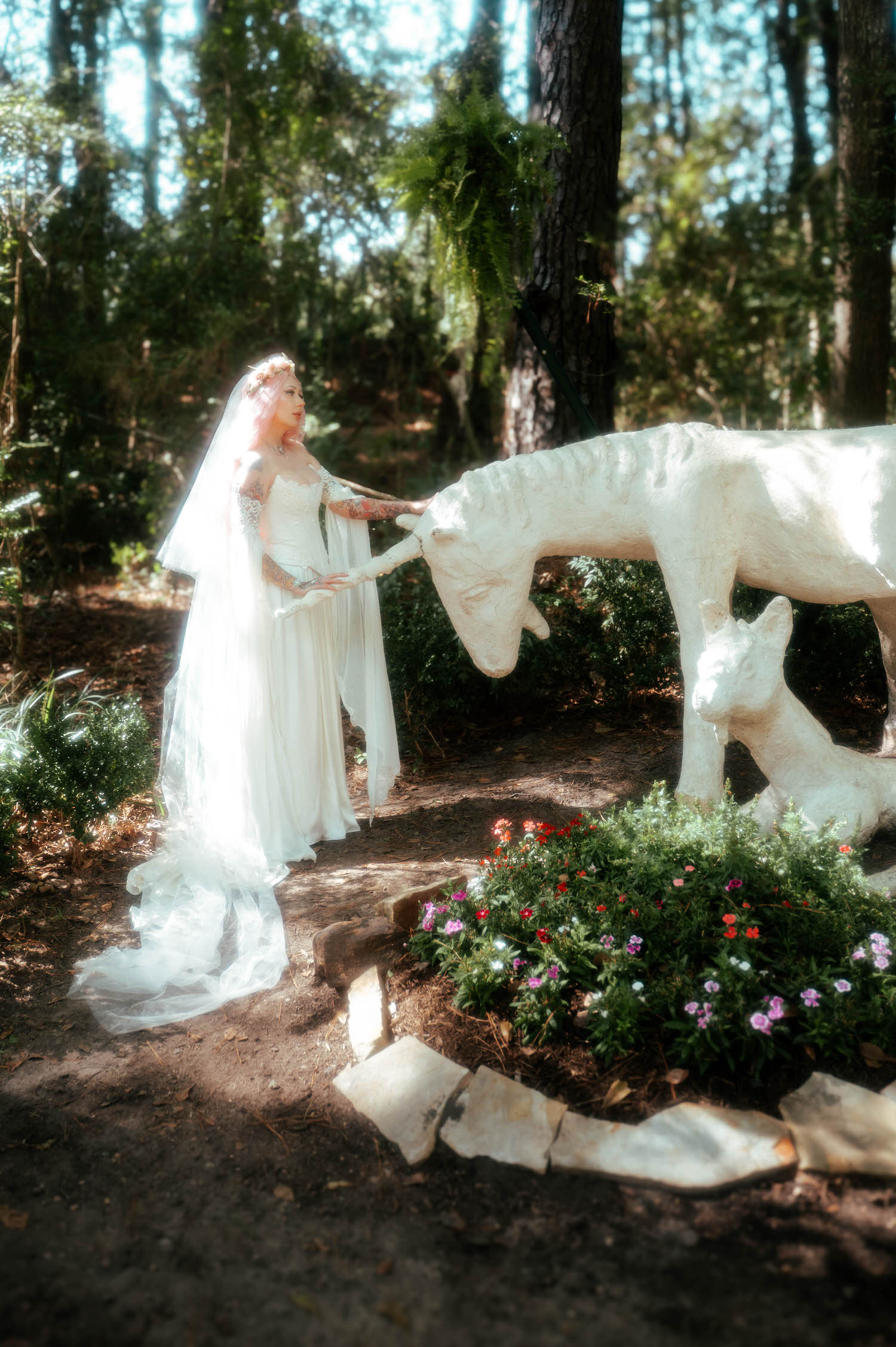 The bride in her Firefly Path bridal gown reaches out to touch a weathered white statue of a unicorn and fawn in the forest, her veil trailing behind her. Magical details like this make this venue a dream for a fantasy wedding photographer. Royal Lune Photo.