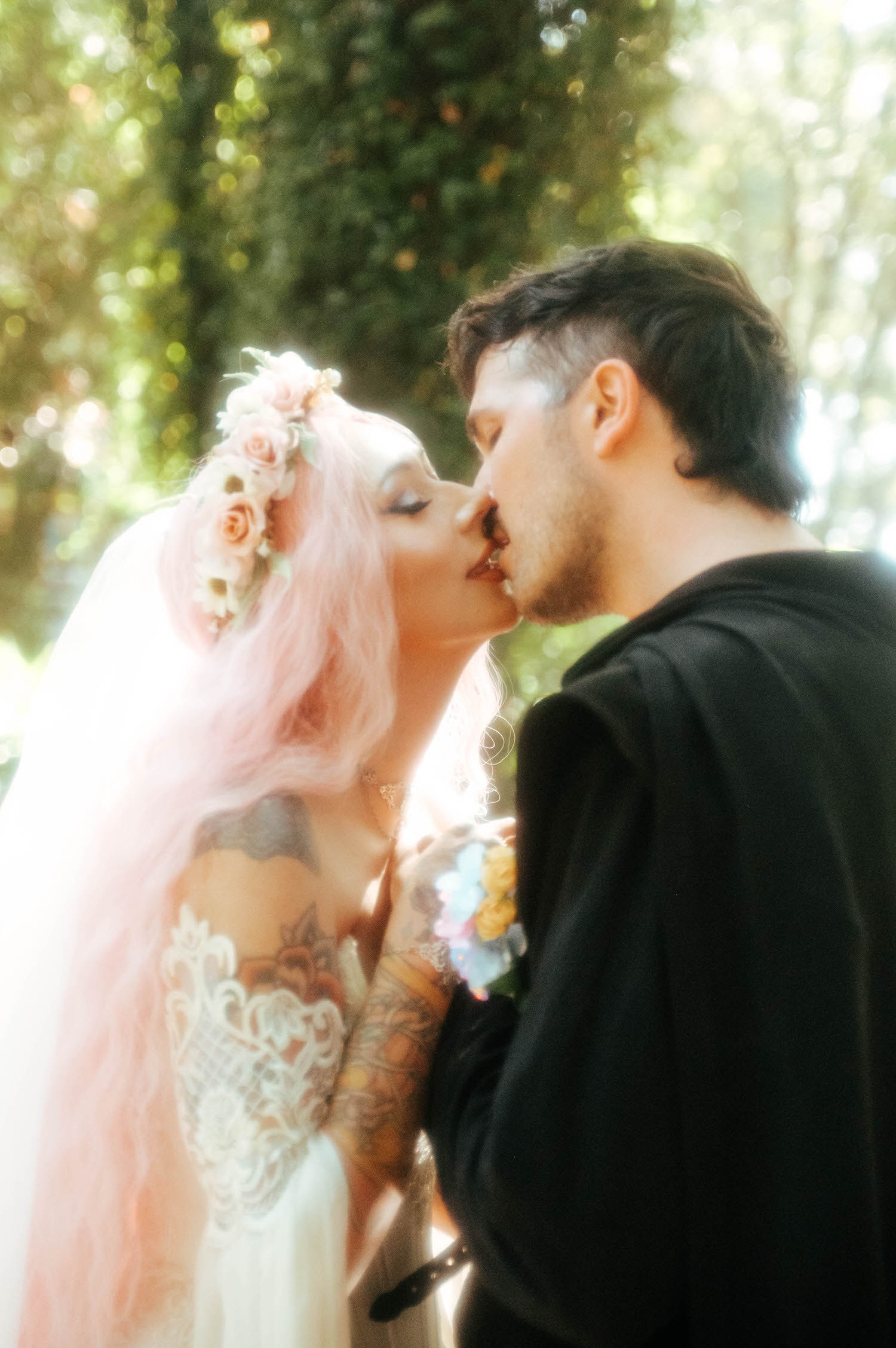 The bride and groom share a tender kiss in close up, her pink hair and floral crown filling the frame in warm sunlight. Close, candid shots like this capture the emotional core of a Texas Renaissance Festival wedding. Royal Lune Photo.
