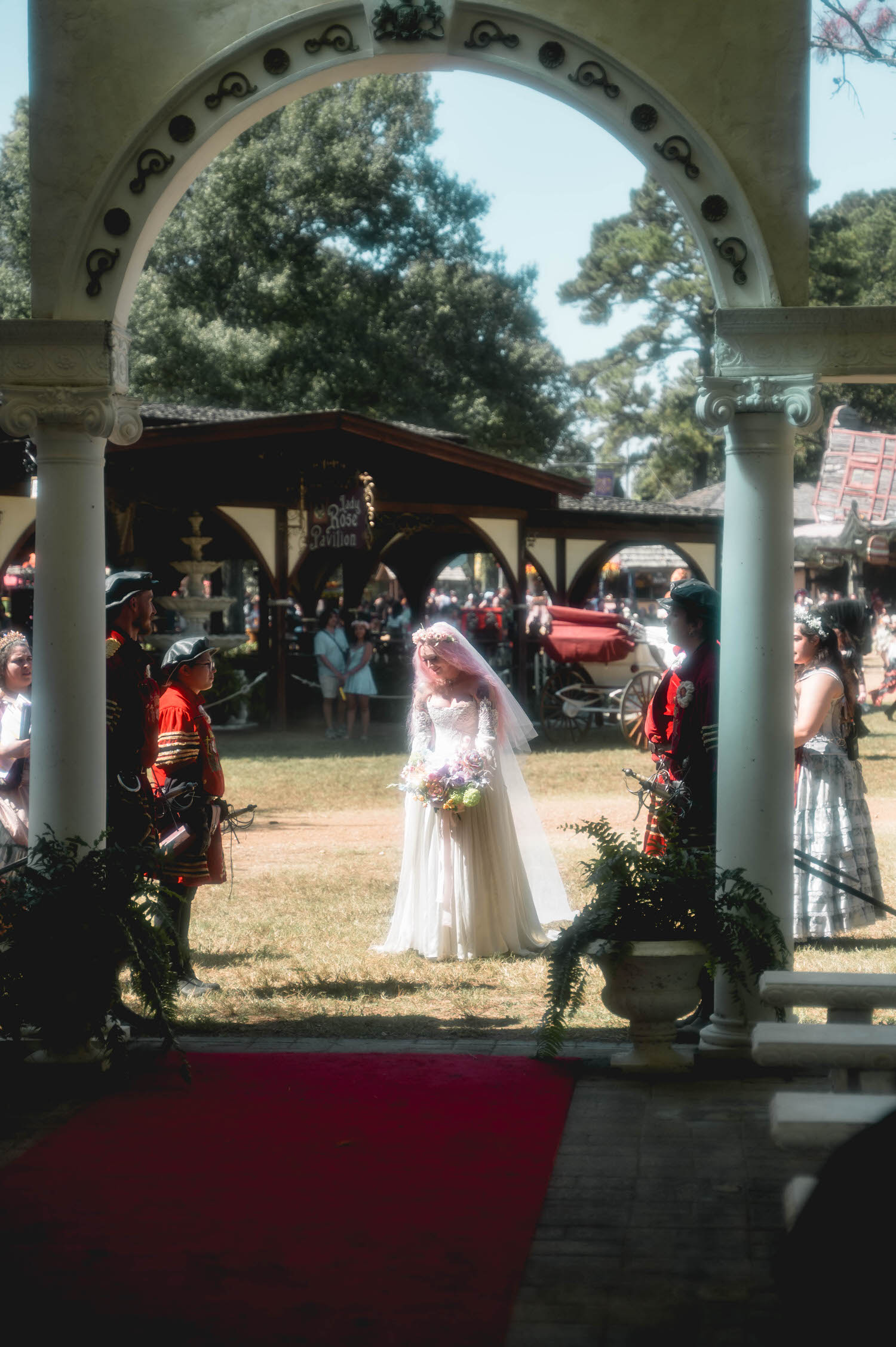 Framed beneath the stone archway of the Italian Village, the bride walks toward her ceremony past festival guards in red and black livery. This dramatic architectural framing is one reason couples seek out a Texas Renaissance Festival wedding photographer. Royal Lune Photo.