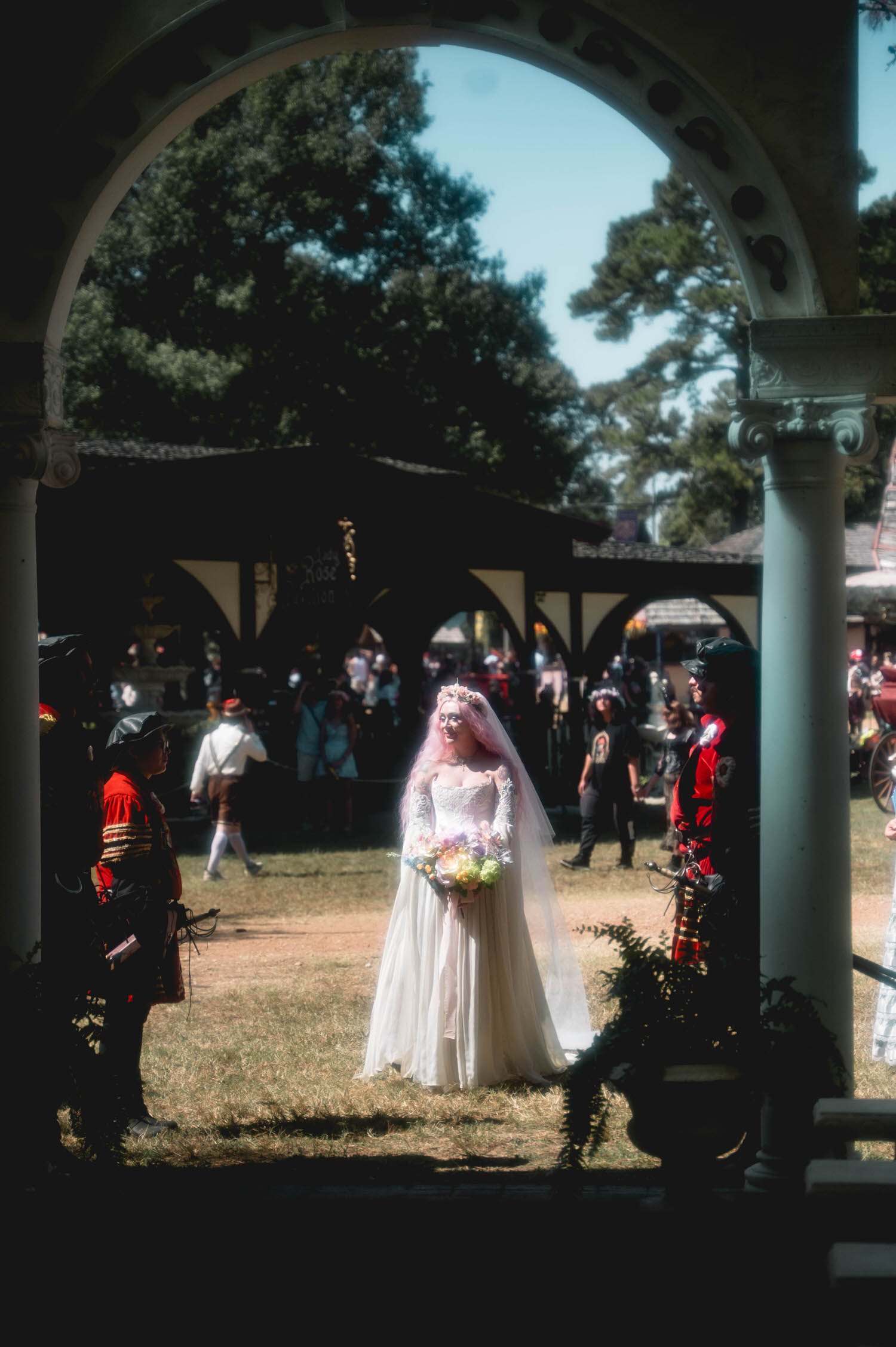 The bride in her Firefly Path Bridal Gown walks down the red carpet toward the altar as a trumpet player announces her arrival under the chapel pavilion. This processional moment captures the festival pageantry that makes a Texas Renaissance Festival wedding so memorable. Royal Lune Photo.
