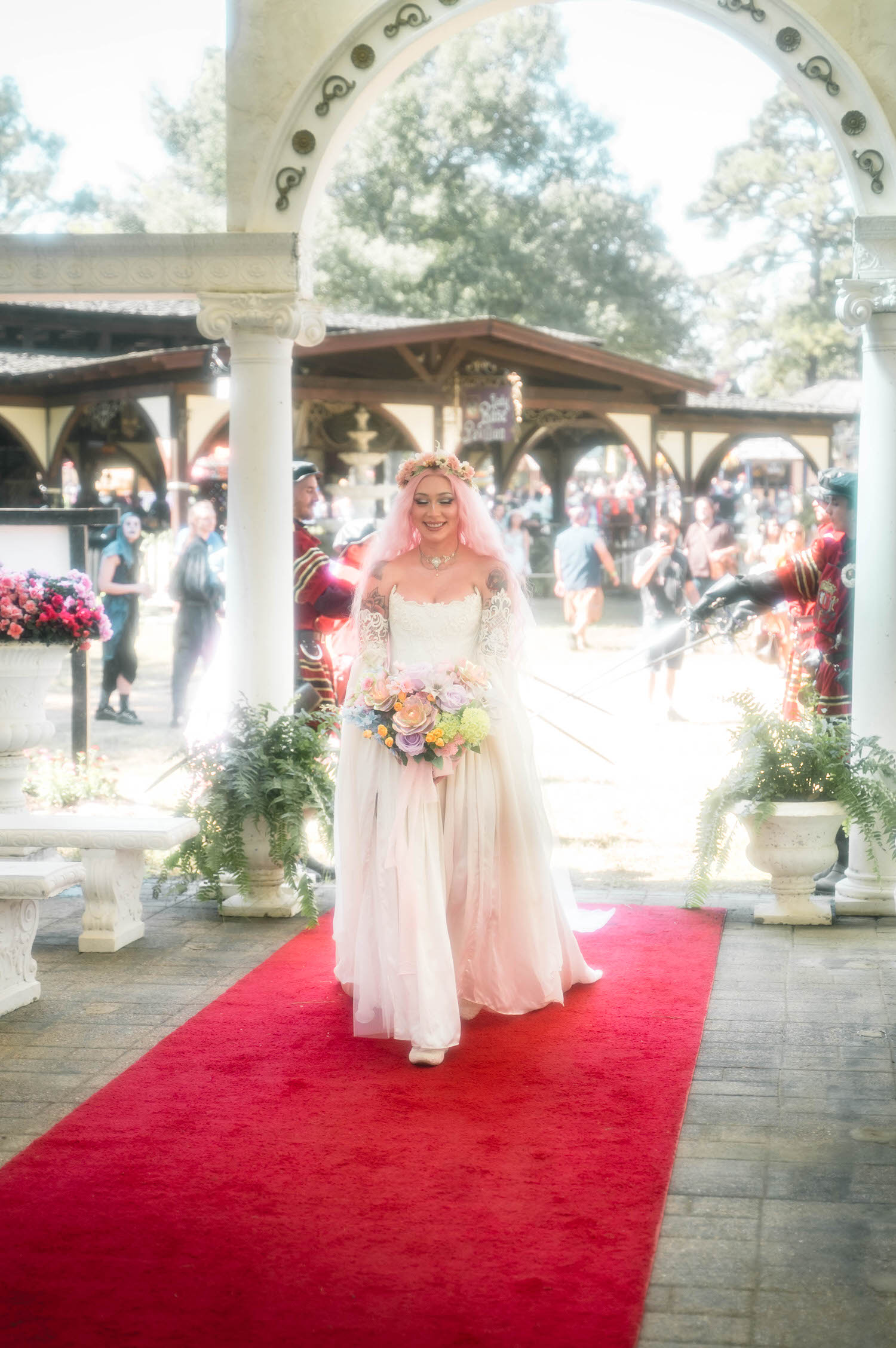 The bride smiles softly while walking the red carpet toward the altar, her flower crown and pink hair glowing in the sunlight as her bouquet catches the light. Moments like this are why couples search for a Texas Renaissance Festival wedding photographer who can capture the romance of the day. Royal Lune Photo.