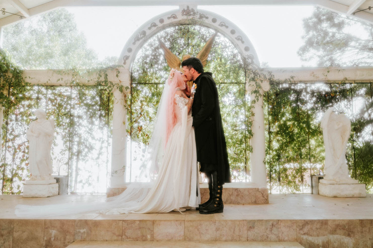 The bride and groom share their first kiss beneath the white archway at the Basilica Wedding Chapel during their Texas Renaissance Festival wedding photographer's session. Royal Lune Photo.