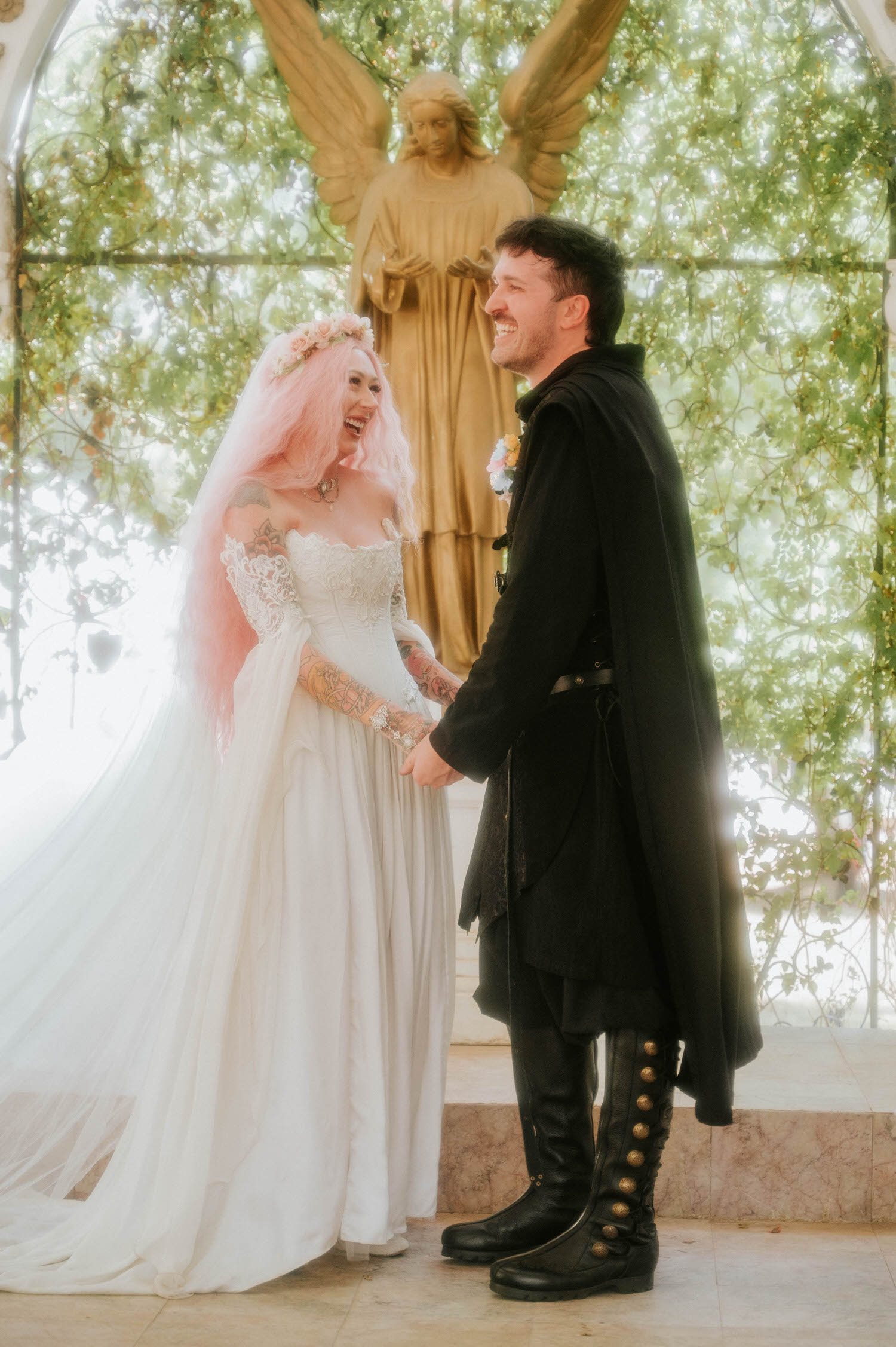 The bride and groom laugh together while holding hands at the altar just after exchanging rings, the angel statue and ivy framing them from behind. Candid joy like this is what makes a Texas Renaissance Festival wedding photographer's job so rewarding. Royal Lune Photo.