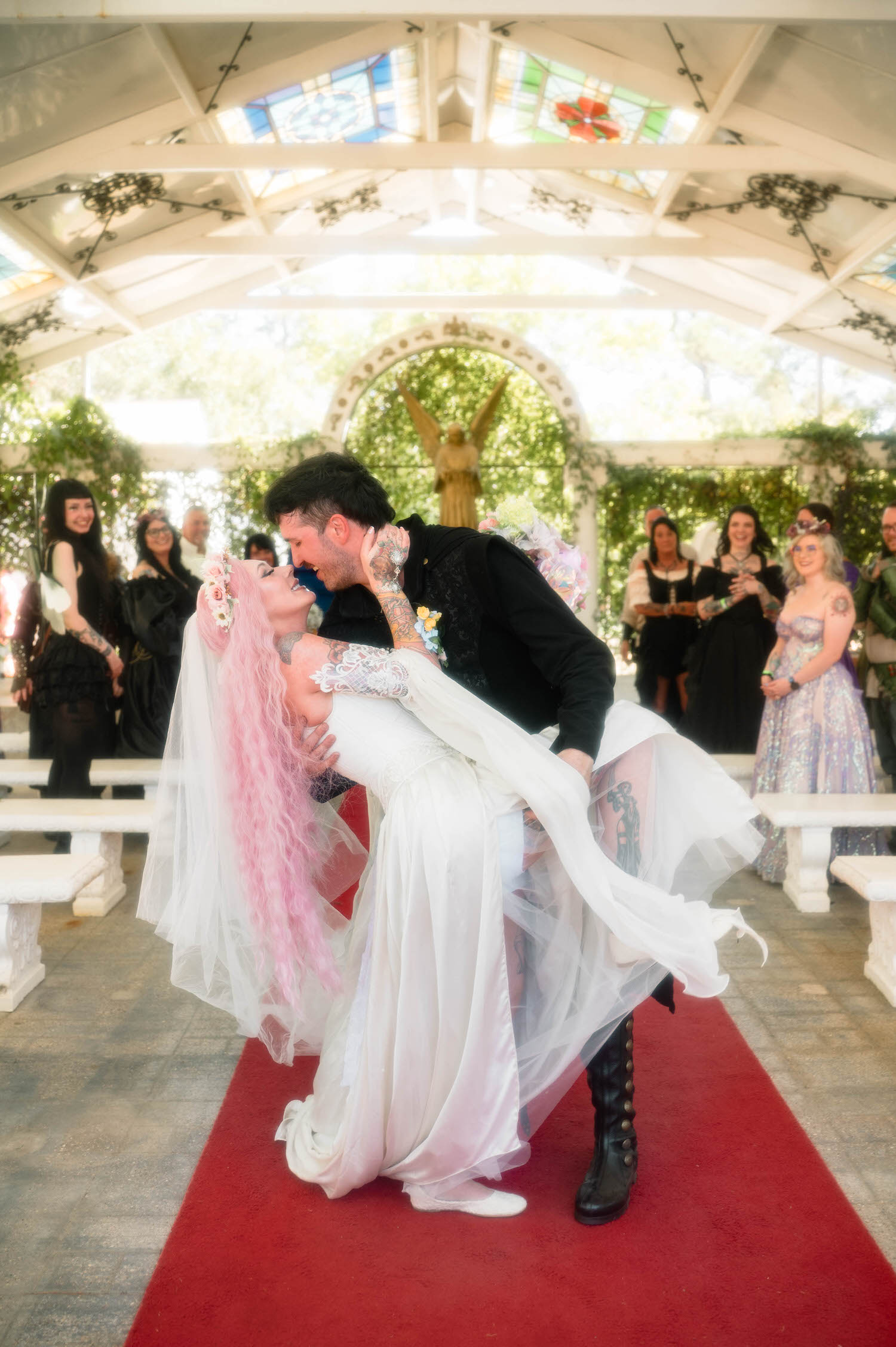 The groom dips the bride for a kiss on the red carpet aisle as cheering guests in elaborate costumes look on from the white stone benches. This playful, theatrical moment is exactly what makes a Renaissance festival wedding so much fun to photograph. Royal Lune Photo.