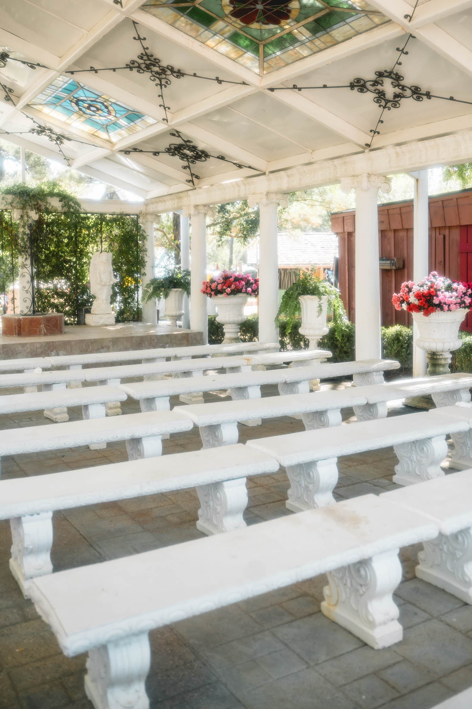 Rows of white stone benches lead toward the altar beneath a stained glass ceiling at the Basilica Wedding Chapel before guests arrive. The empty aisle captures the elegant atmosphere couples can expect from their Texas Renaissance Festival wedding photographer. Royal Lune Photo.