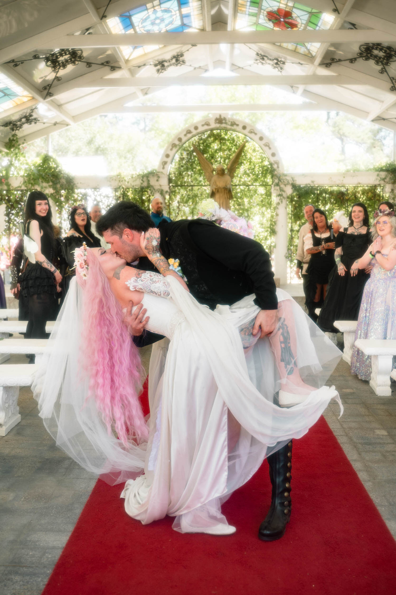 The newlyweds share a dramatic dip and kiss down the aisle, the bride's tattooed leg peeking through her gown as delighted guests applaud on either side. Bold, unforgettable moments like this are why couples choose a Texas Renaissance Festival wedding photographer who can capture their personality. Royal Lune Photo.