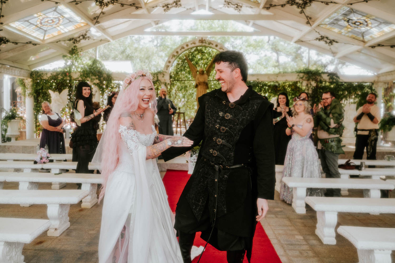 The newlyweds laugh together while recessing down the aisle as cheering guests in Renaissance costumes applaud on either side of the chapel. This joyful exit captures the celebratory spirit of a Texas Renaissance Festival wedding. Royal Lune Photo.