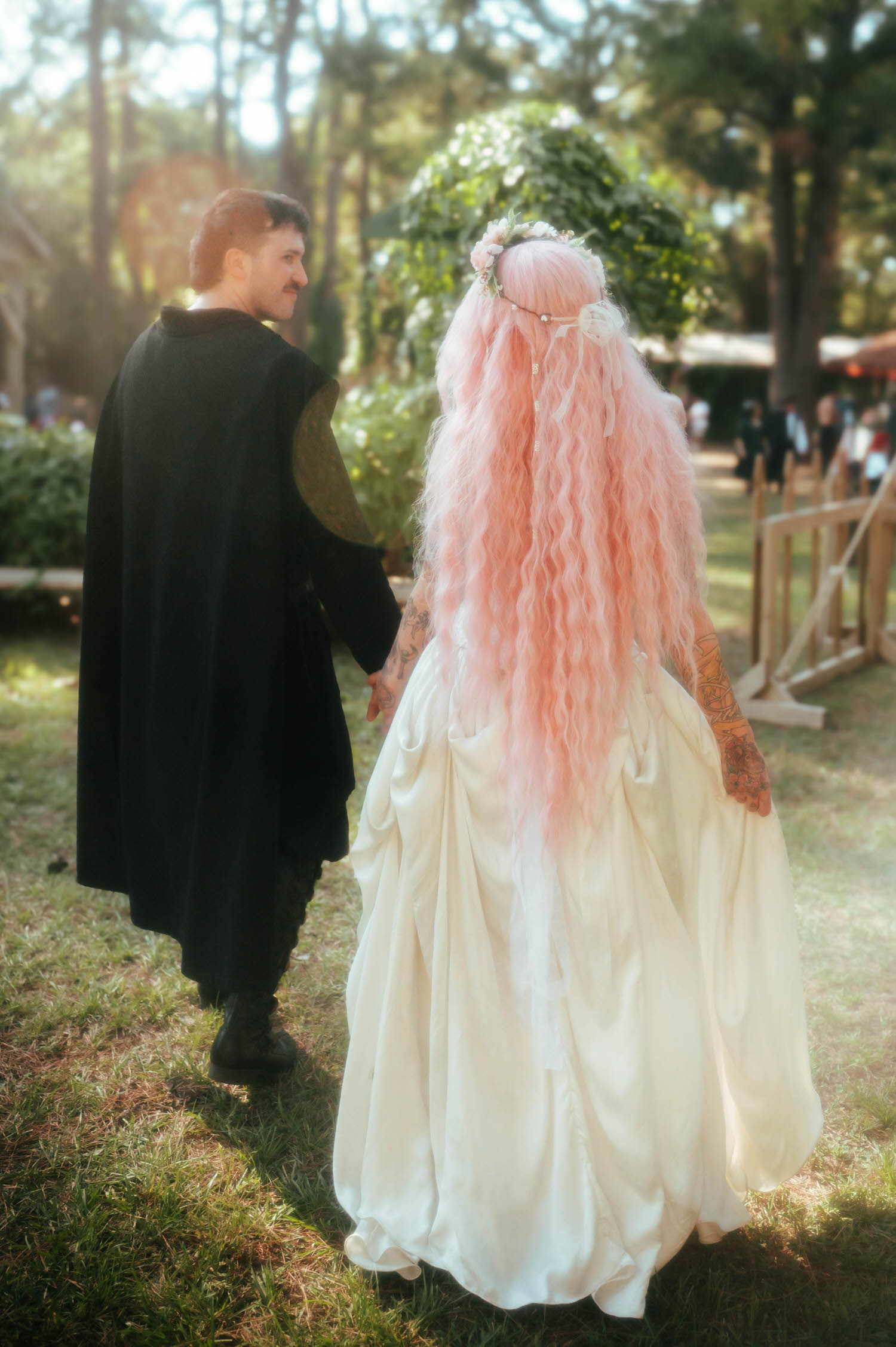 The groom in a black cloak walks beside his bride through the festival grounds following their Renaissance festival wedding reception at the Italian Village. Royal Lune Photo.