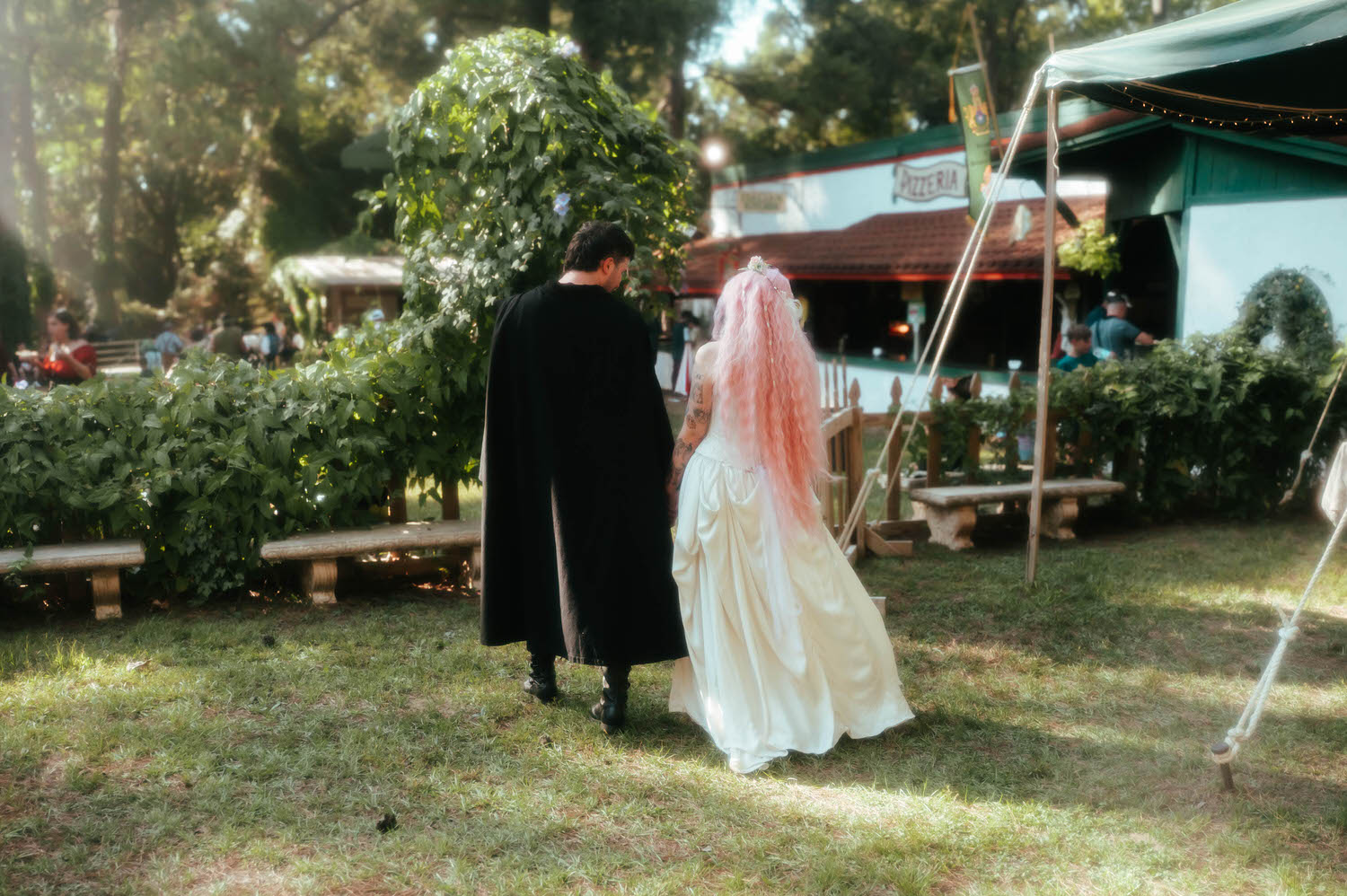 The newlyweds stroll past festival tents and a pizzeria storefront, blending Renaissance charm with the lively atmosphere of the fair. Royal Lune Photo.