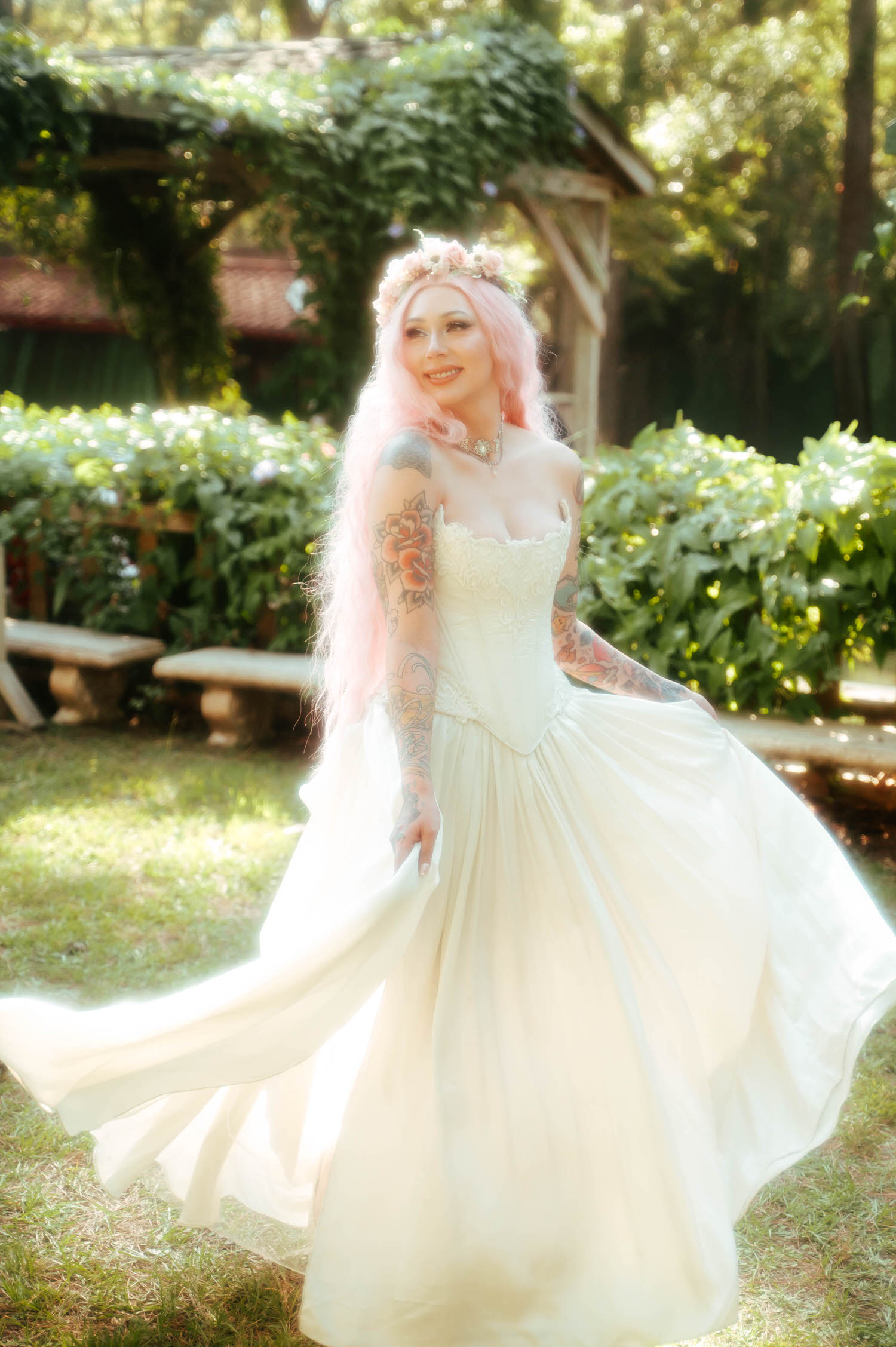 The bride poses in her Firefly Path Bridal Gown with rose tattoos visible on her arm and a flower crown resting on her pink hair. Royal Lune Photo.