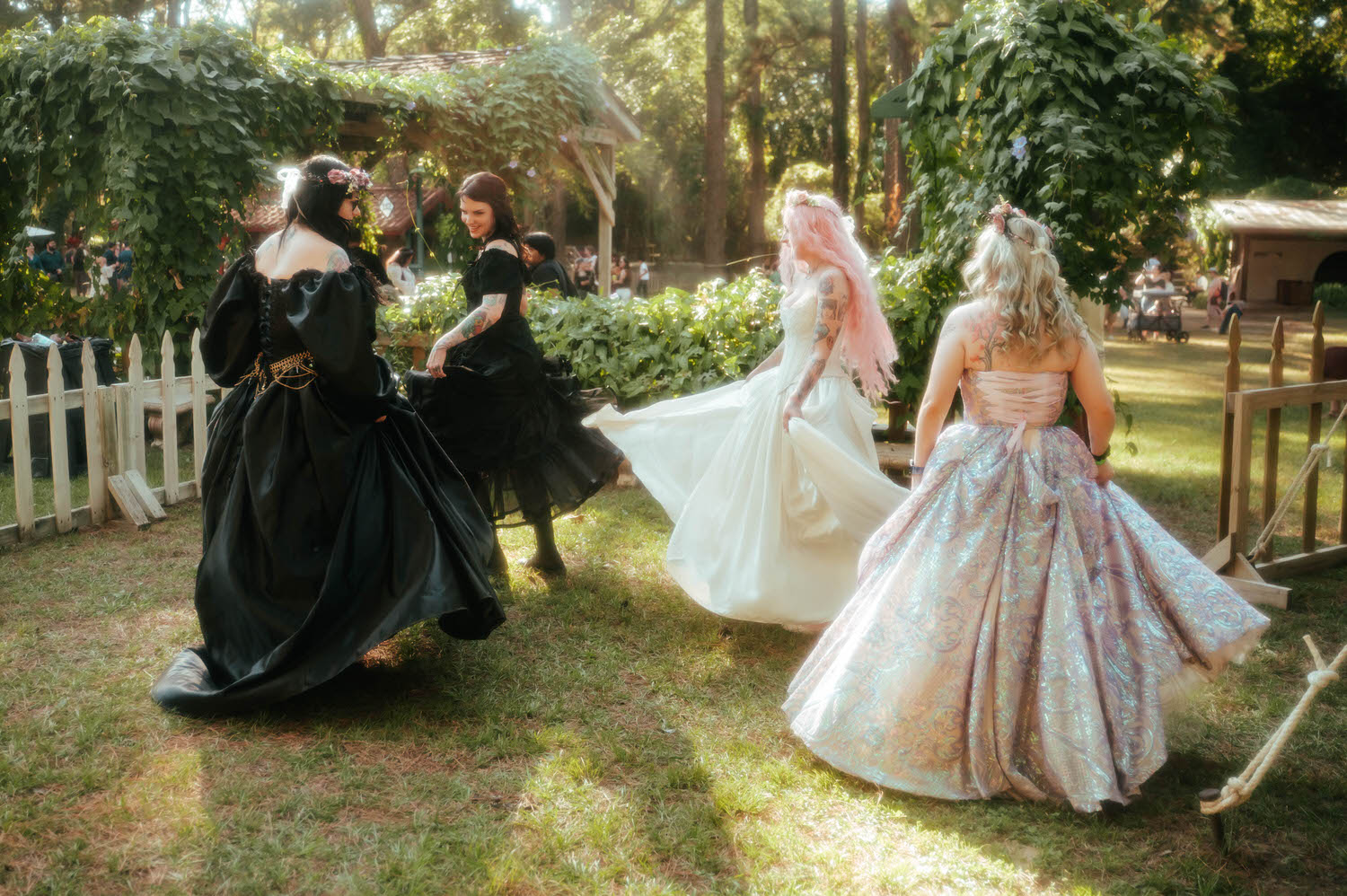 Bridesmaids in black Renaissance gowns and a shimmering iridescent dress dance alongside the bride at a fantasy wedding photographer's session. Royal Lune Photo.