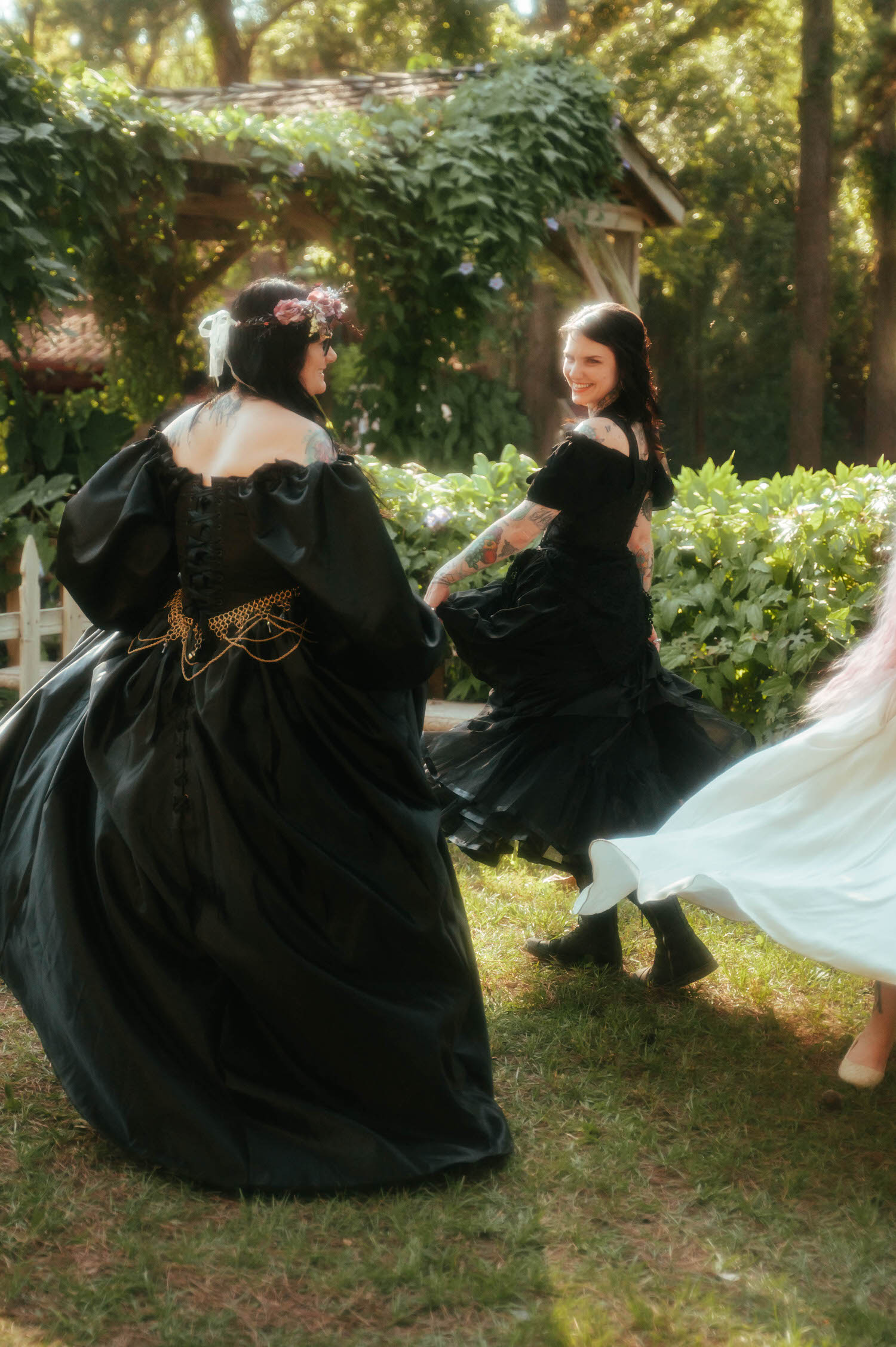 Two bridesmaids in flowing black taffeta gowns laugh and twirl together at a Texas Renaissance Festival wedding photographer's session. Royal Lune Photo.