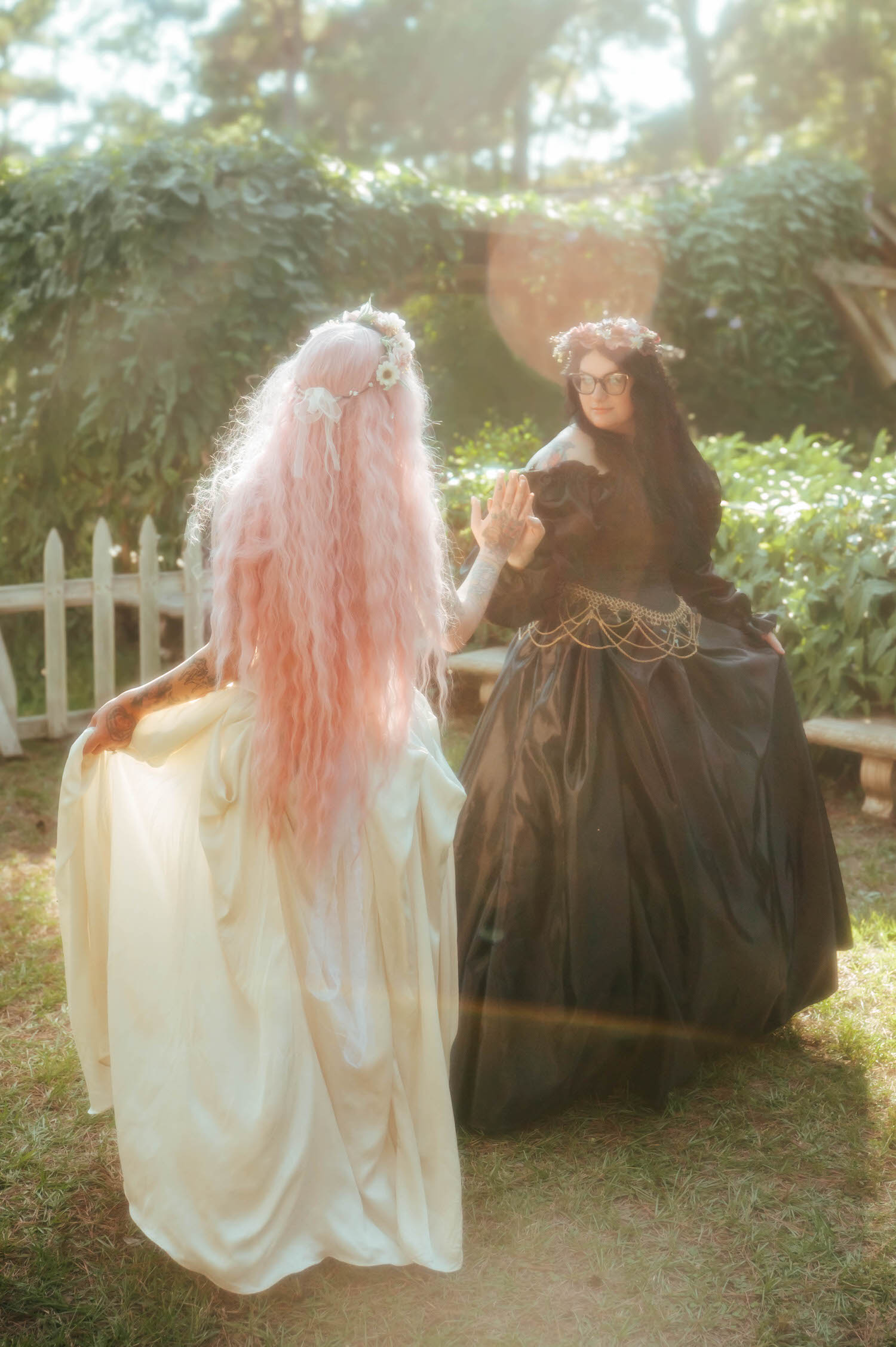 The bride and maid of honor in a black ballgown reach toward each other with playful energy, their pink and dark hair contrasting beautifully in the sunlight. Creative portraits like this showcase the artistic side of a fantasy wedding photographer. Royal Lune Photo.