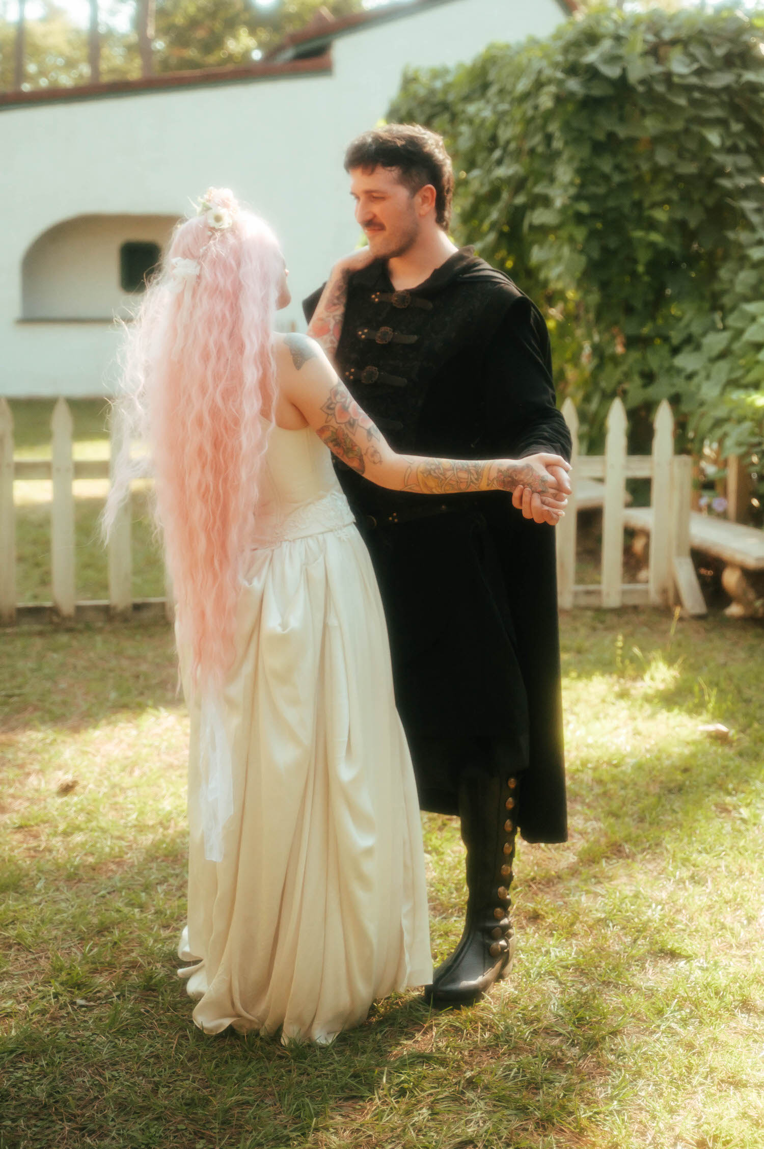 The bride and groom hold hands mid dance, her pink hair flowing as she smiles back at him near the reception fence line. Sweet partner dance moments like this are a favorite for any Texas Renaissance Festival wedding photographer. Royal Lune Photo.