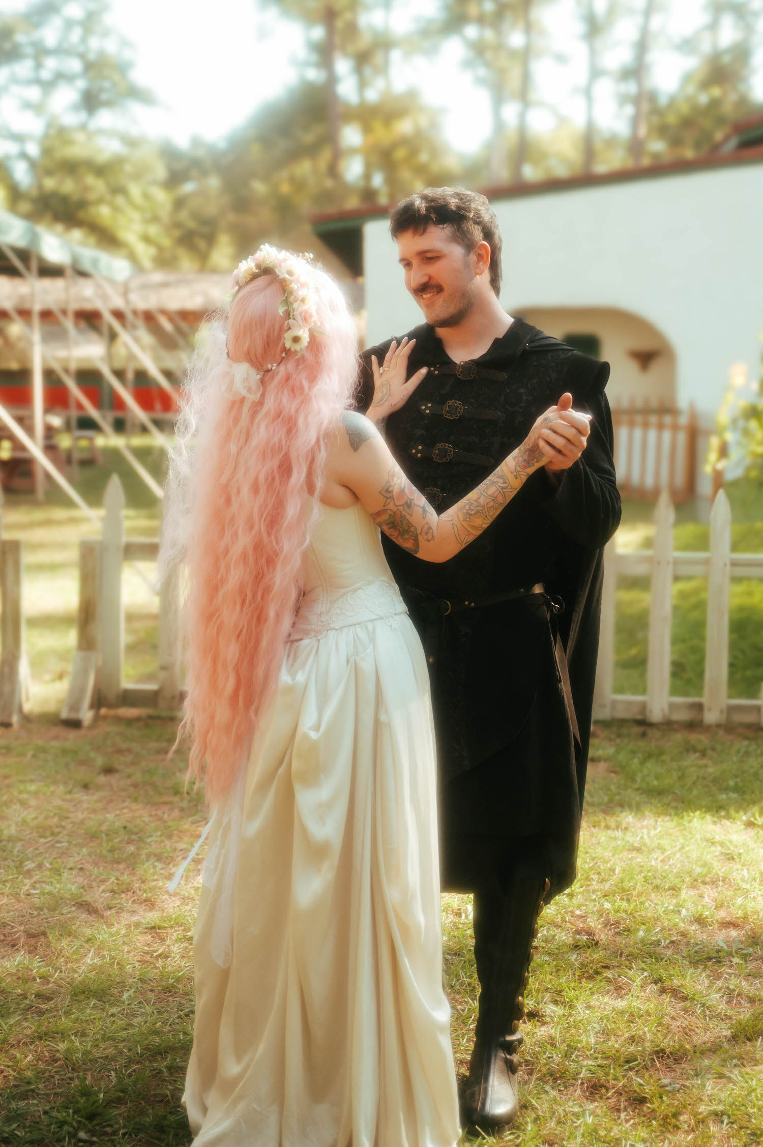 The groom holds the bride close as she smiles up at him, her pink hair and tattooed shoulder glowing in the warm afternoon light. Tender exchanges like this capture the heart of a Texas Renaissance Festival wedding. Royal Lune Photo.