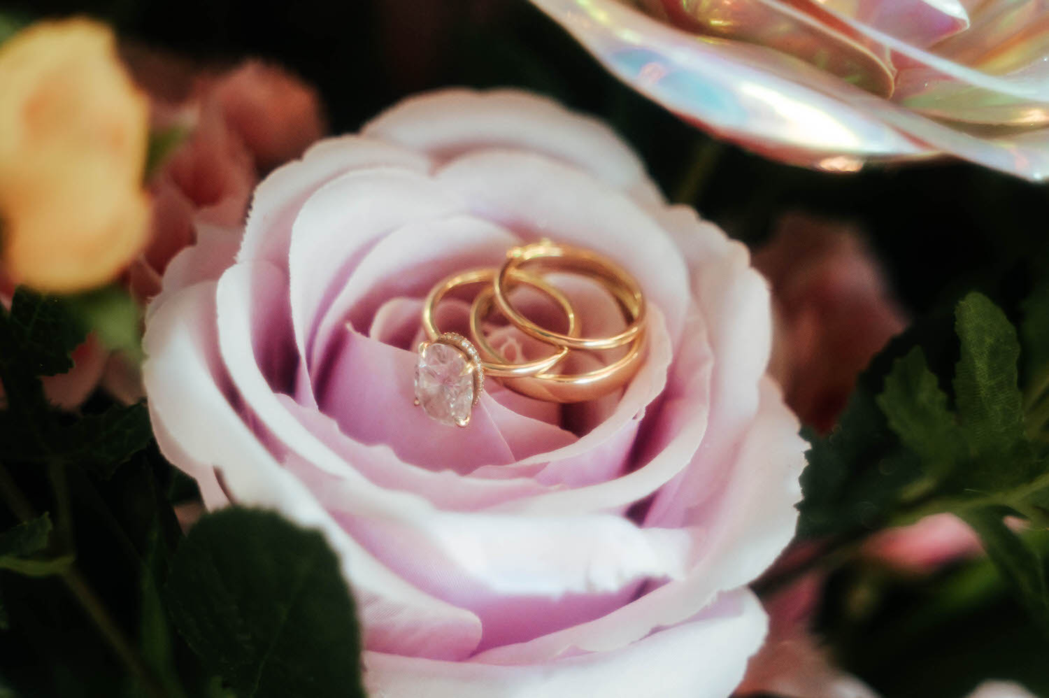 A diamond engagement ring and gold wedding bands rest nestled inside a soft pink rose among the reception florals. Macro details like this are a favorite way to document a Texas Renaissance Festival wedding. Royal Lune Photo.