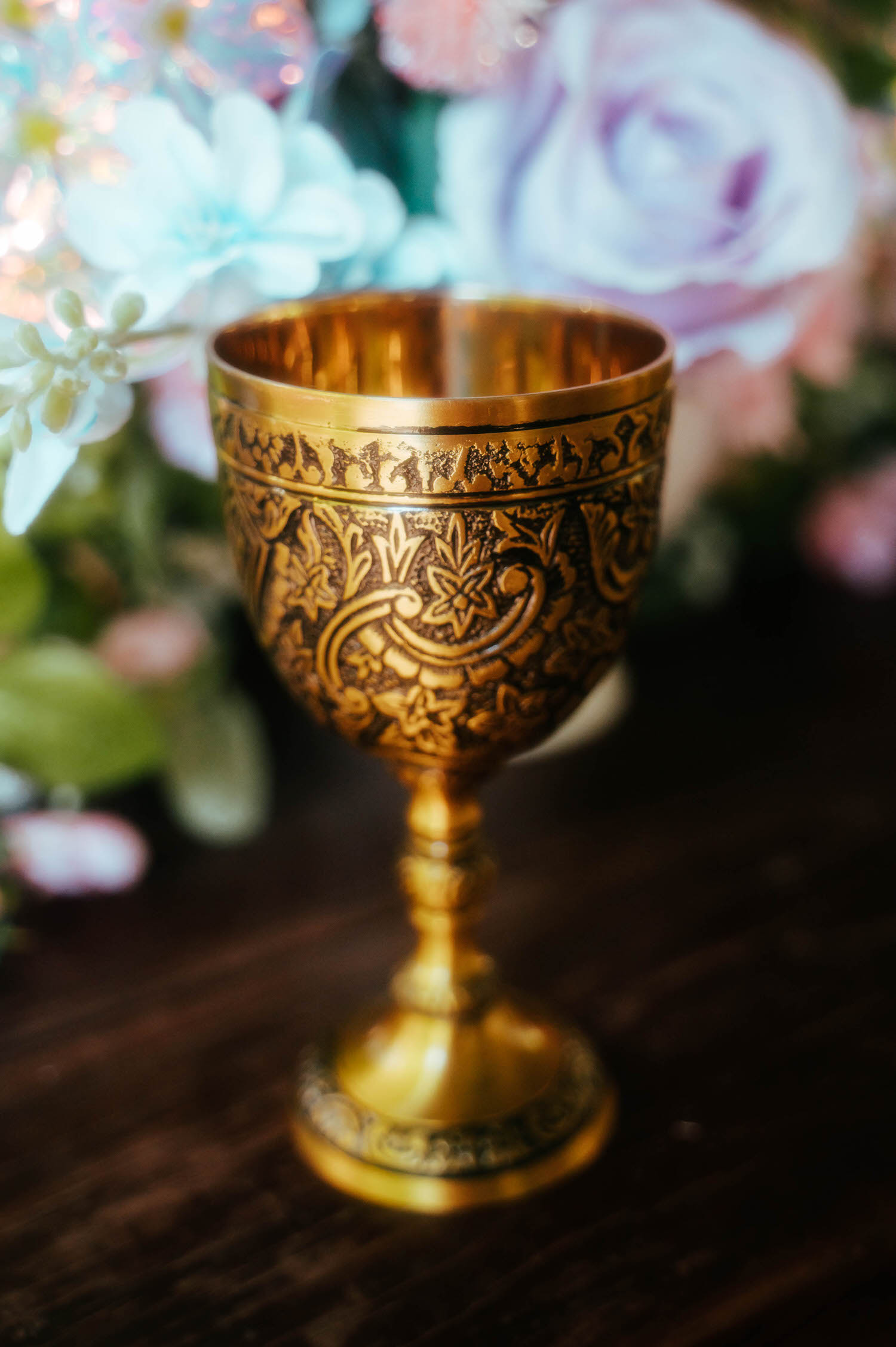 An ornate gold goblet with intricate engraved designs sits on the reception table surrounded by soft pastel florals. Decorative details like this bring an authentic medieval touch to a Renaissance festival wedding. Royal Lune Photo.