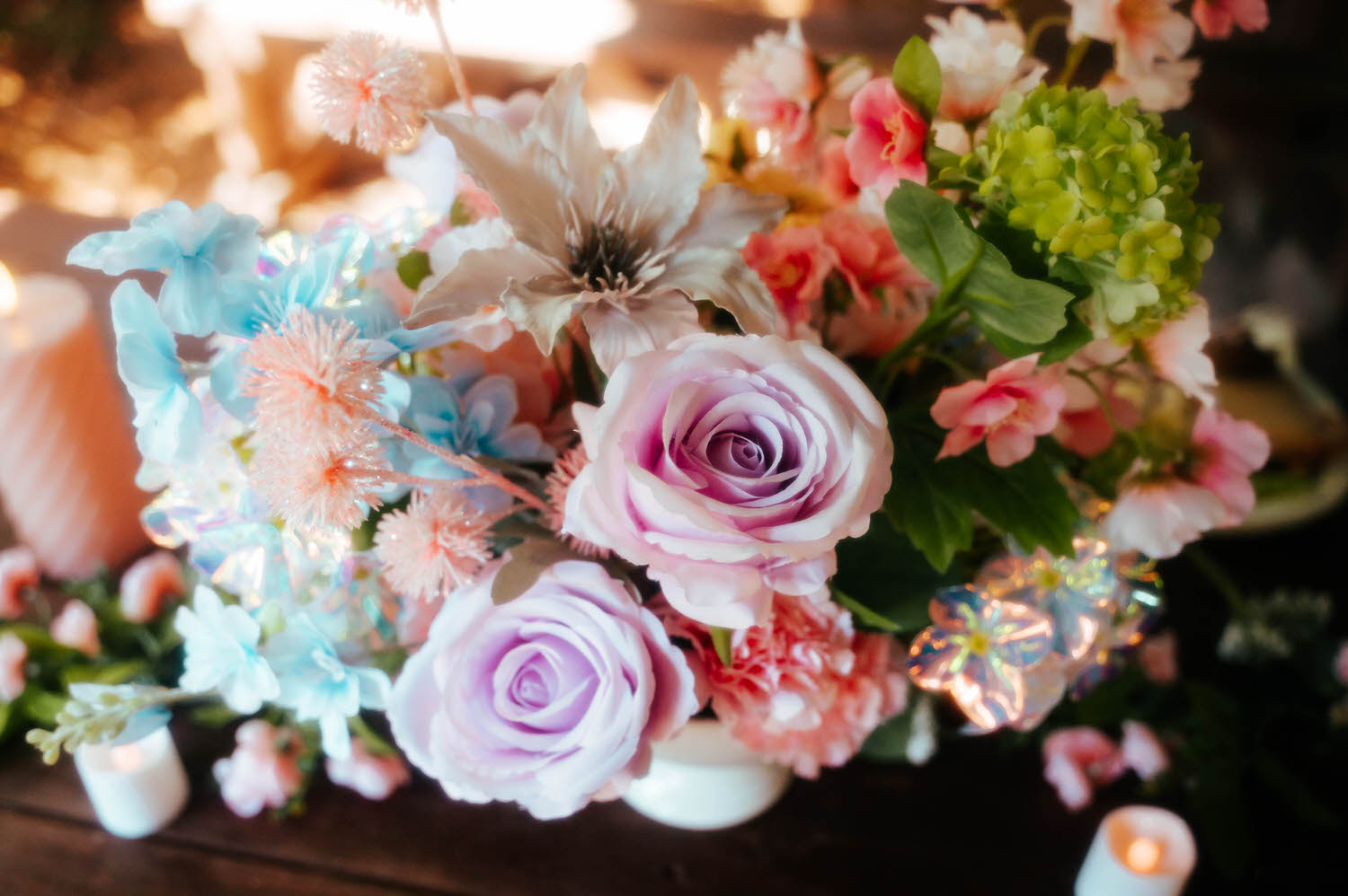 A close up of the reception centerpiece shows lavender roses, blue hydrangea, and pink blooms arranged among iridescent accents and candles. Romantic floral details like this elevate every Texas Renaissance Festival wedding. Royal Lune Photo.