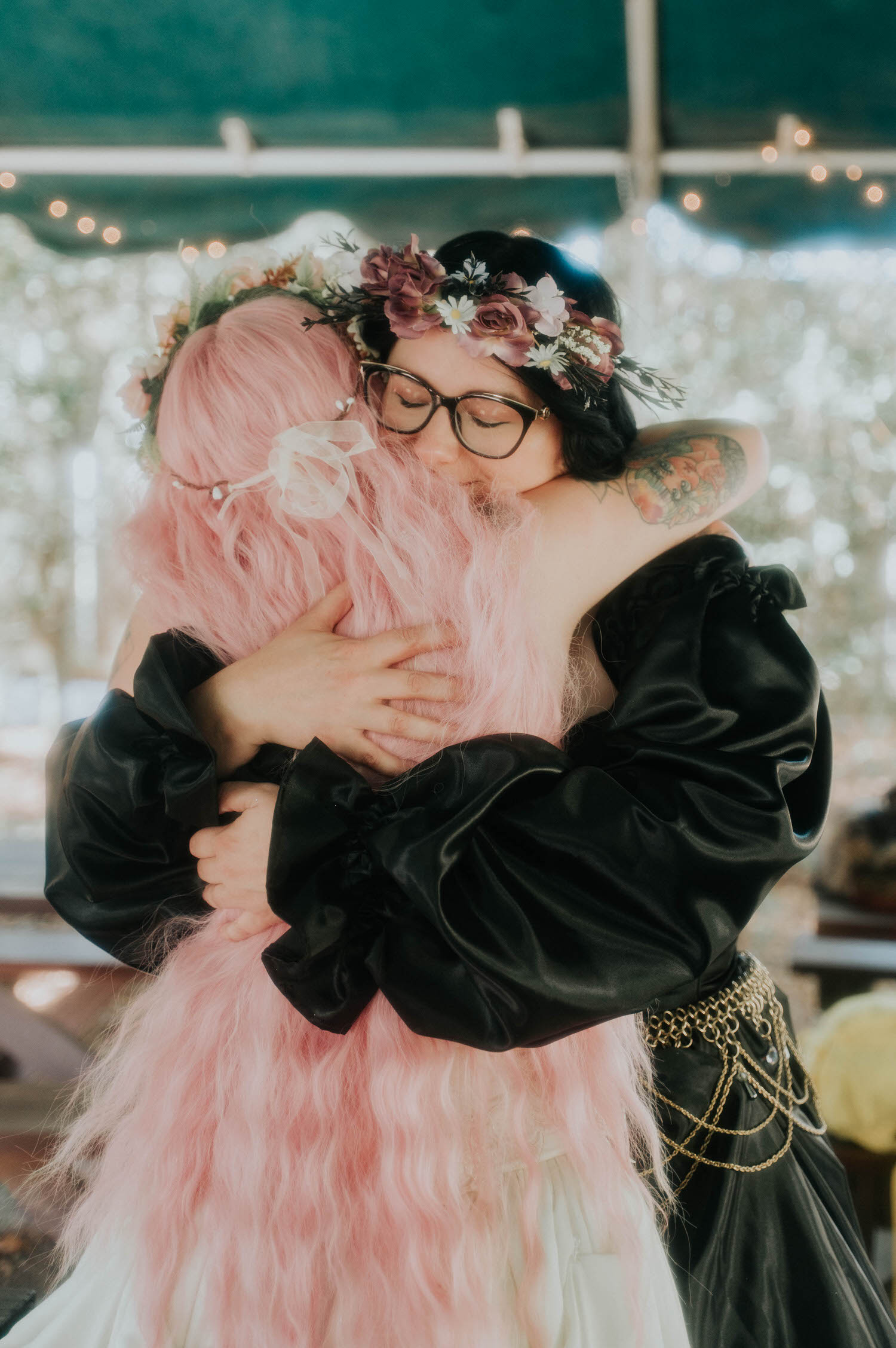 The bride embraces a guest in a flower crown and black gown in a warm, close hug at the reception. Heartfelt moments like this capture the love surrounding a Texas Renaissance Festival wedding. Royal Lune Photo.