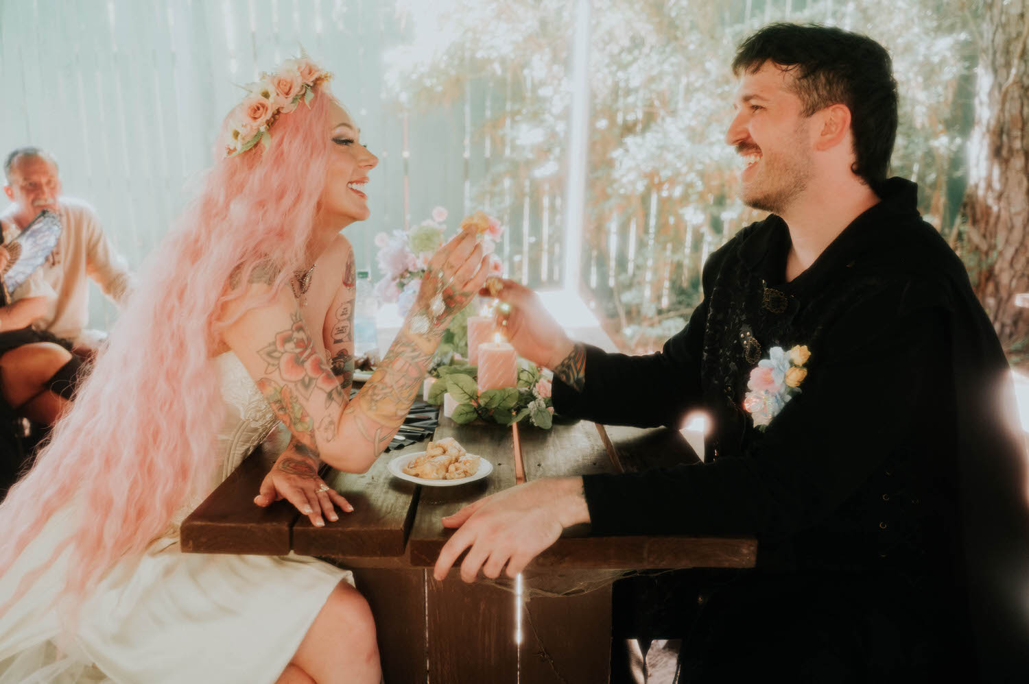 The bride feeds the groom a bite of funnel cake at the reception table, both laughing together in the warm afternoon light. Playful moments like this capture the fun loving spirit of a Texas Renaissance Festival wedding. Royal Lune Photo.