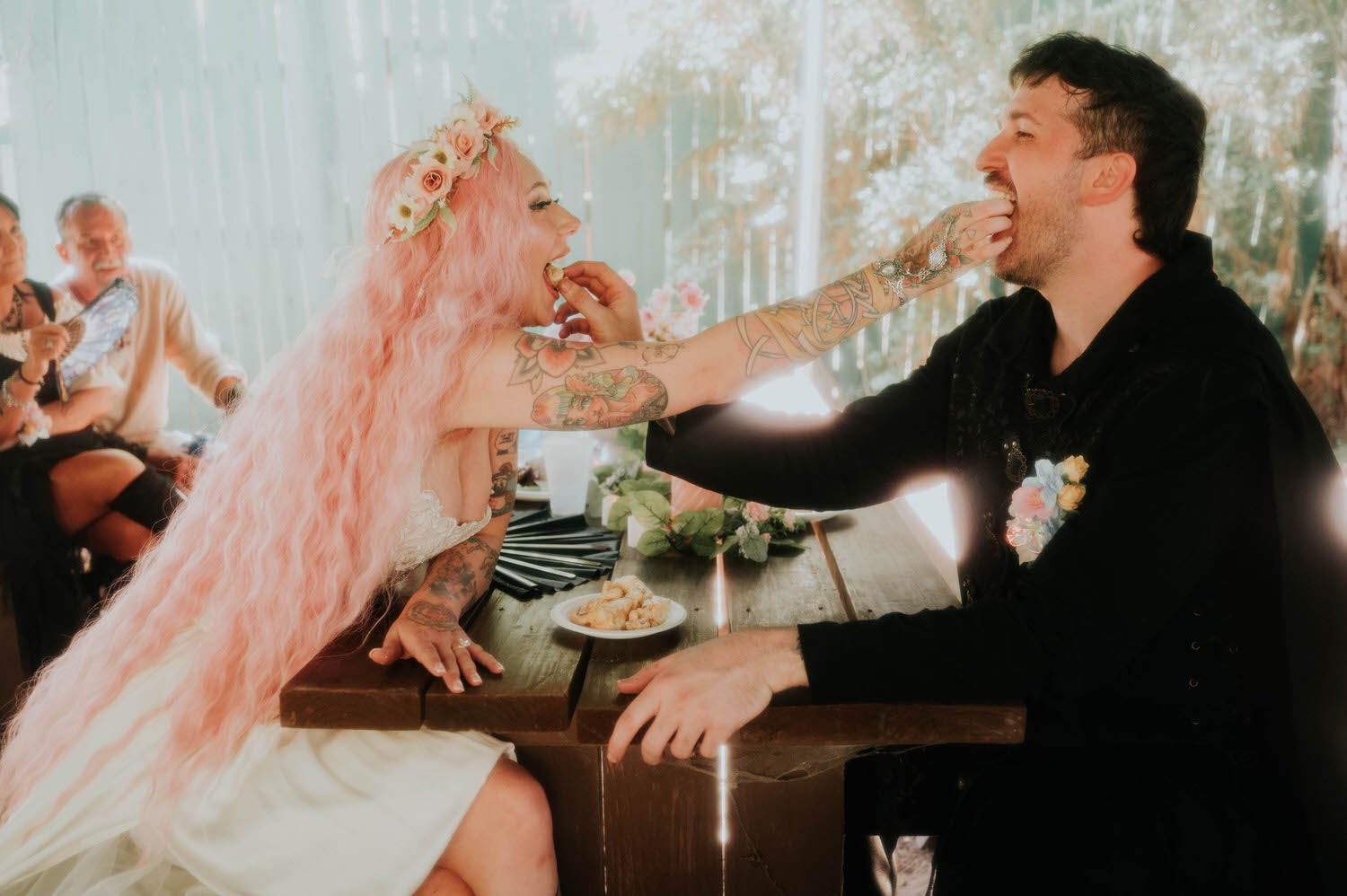 The bride feeds the groom another bite of funnel cake, her pink hair catching the light as they share a laugh at their reception table. Sweet, candid exchanges like this are a favorite part of documenting a Texas Renaissance Festival wedding. Royal Lune Photo.