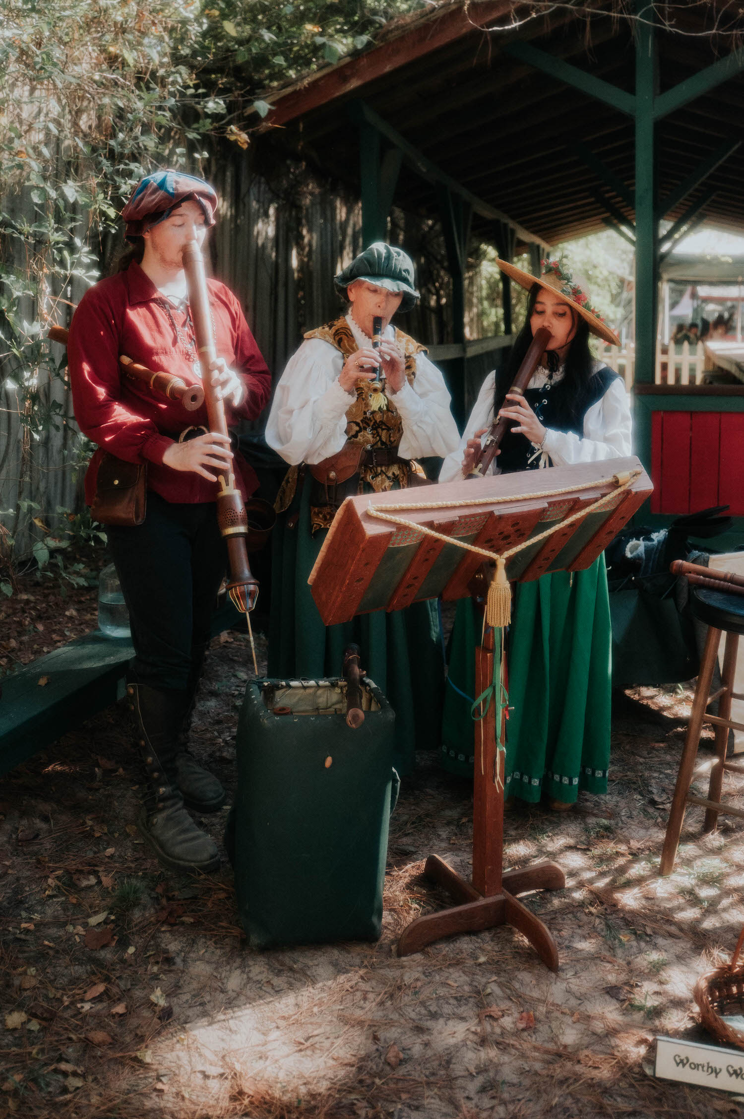 Three musicians in Renaissance attire play wooden recorders and a krummhorn beside a rustic music stand at the reception. Live entertainment like this brings authentic festival charm to a Texas Renaissance Festival wedding. Royal Lune Photo.