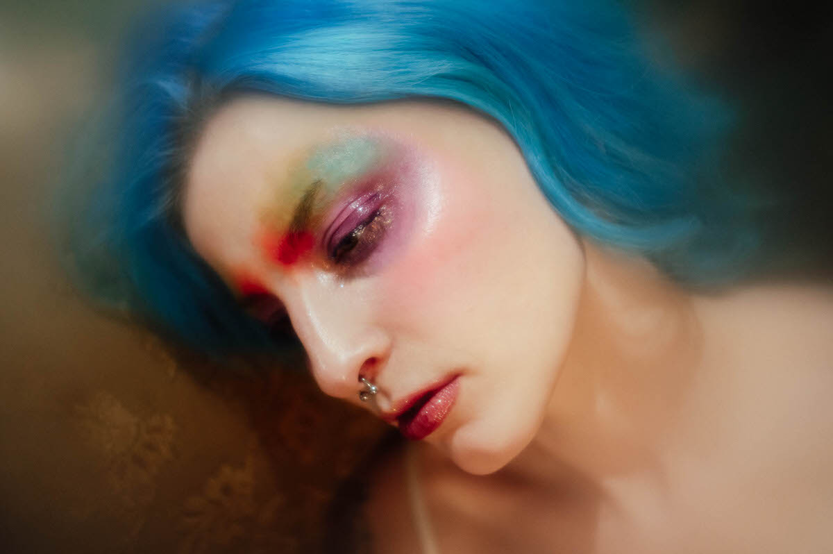 Close up portrait of a woman with blue hair and watercolor style eyeshadow blended in yellow, pink, and purple, taken during a creative portrait photography session at Royal Lune Photo.