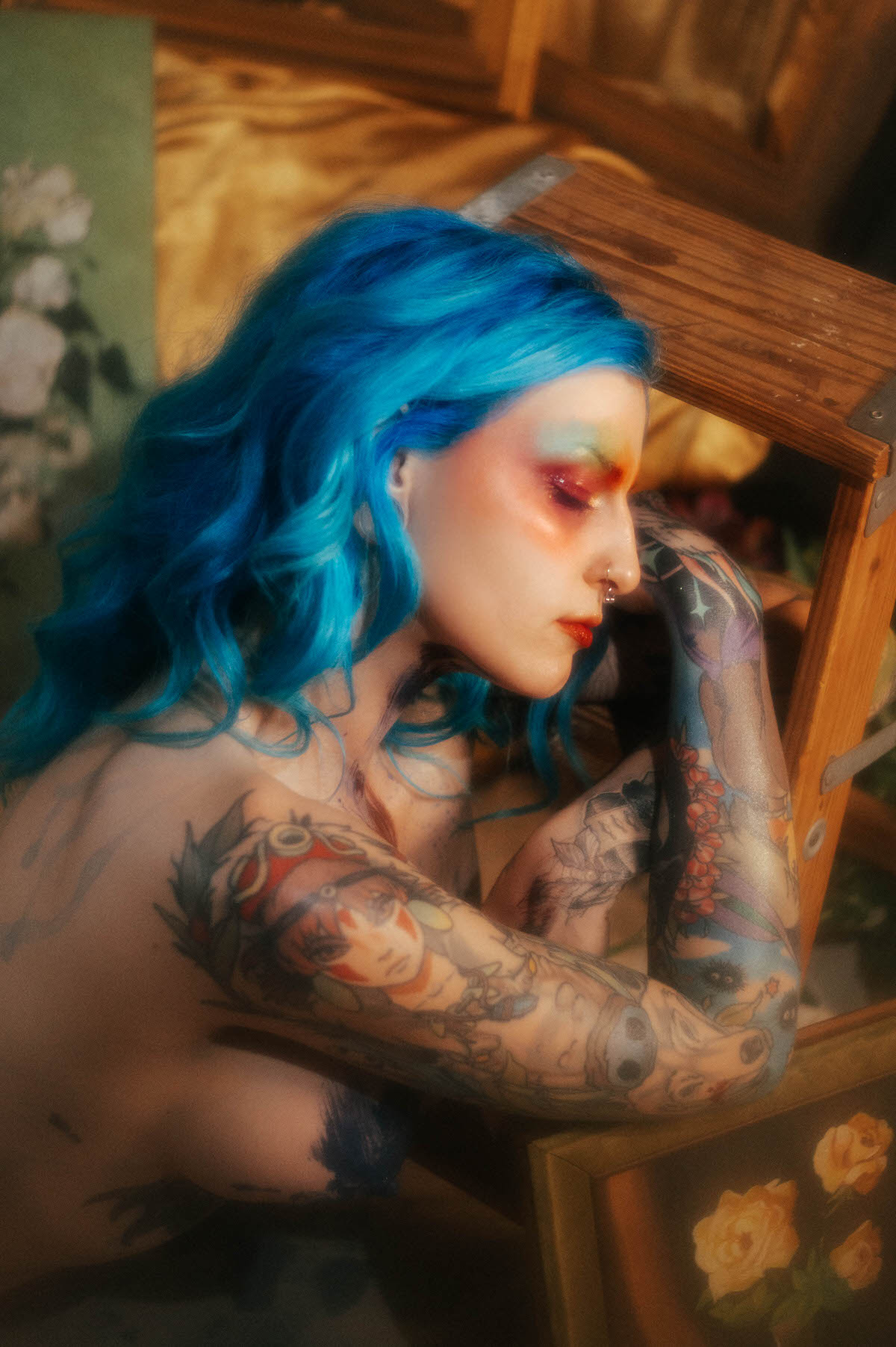 Close crop profile portrait of a woman with blue hair leaning against a wooden ladder rung, a dark paint smudge near her collarbone, during this fine art nude photography session at Royal Lune Photo.