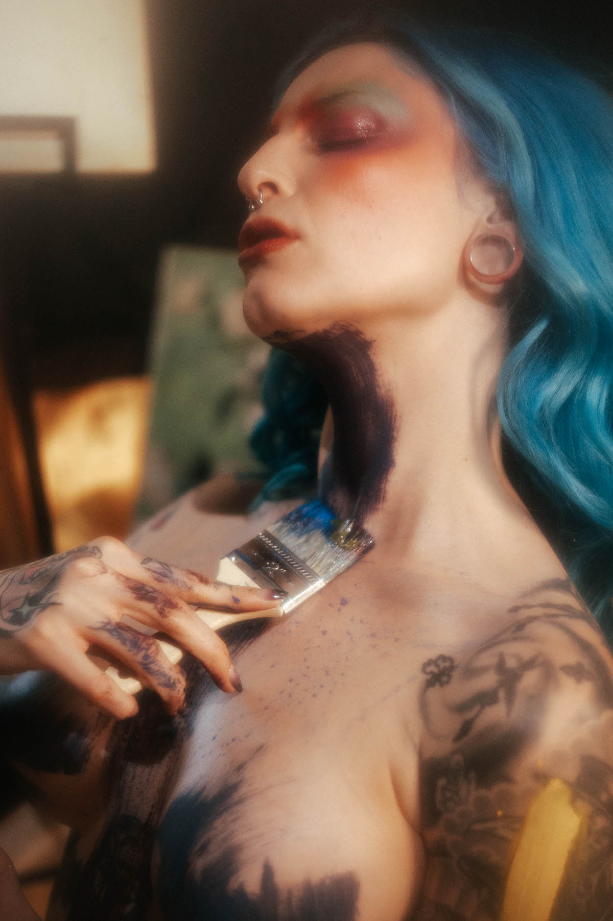 Close up profile portrait of a woman with blue hair and a dark paint stripe on her neck, brush in hand mid stroke, photographed by a Dallas fine art photographer at Royal Lune Photo.
