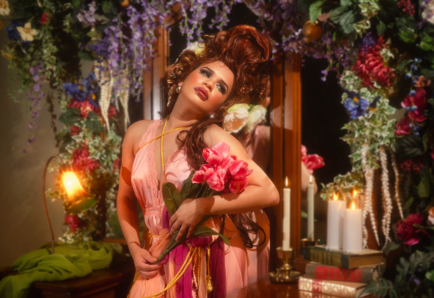 Woman resting against an antique wooden vanity holding pink tulips surrounded by candlelight and floral garland in this fine art photo studio setting, Royal Lune Photo.