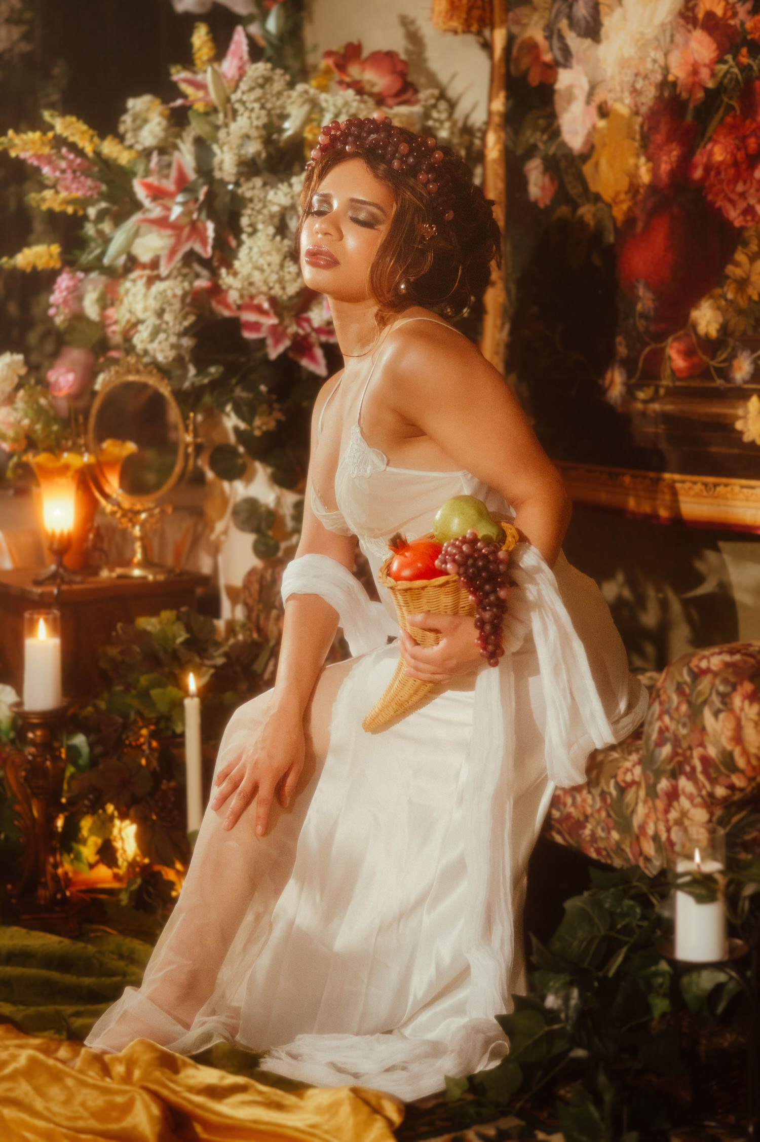 Woman with a grape crown wig holding a woven basket of grapes and pomegranate in this art nouveau photography session set against a lush floral backdrop, Royal Lune Photo.