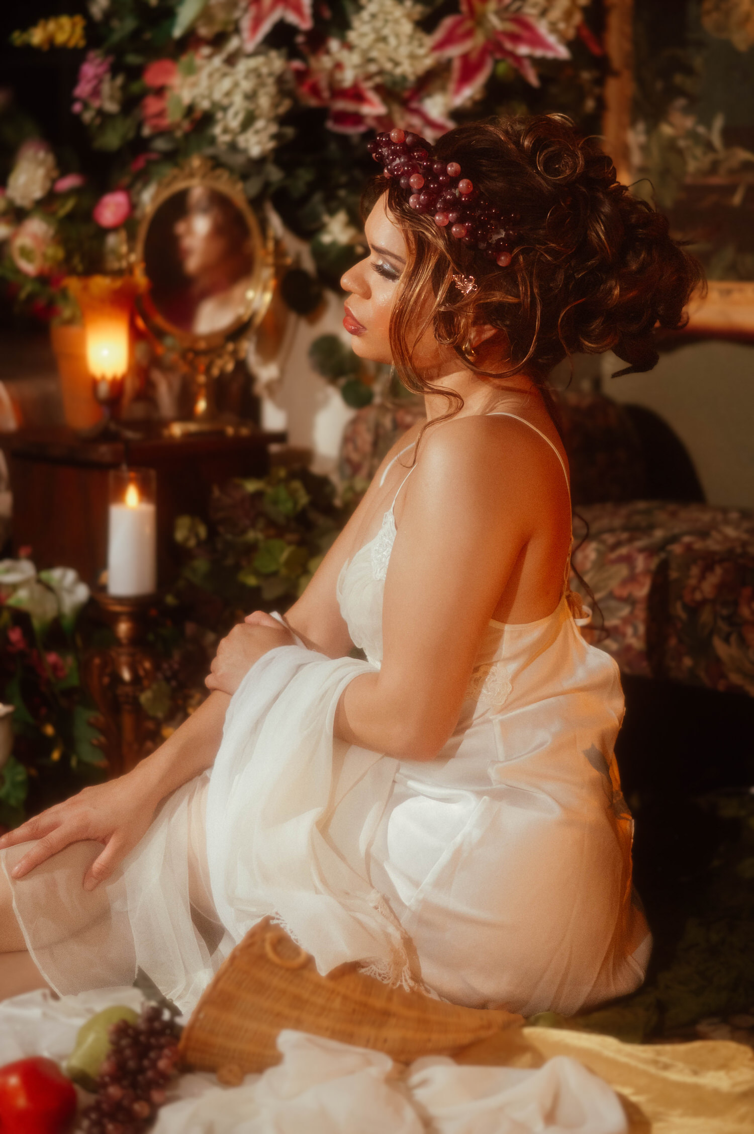 Woman in profile wearing a vintage nightgown and grape crown wig seated beside an antique vanity mirror and lit candles, Royal Lune Photo.