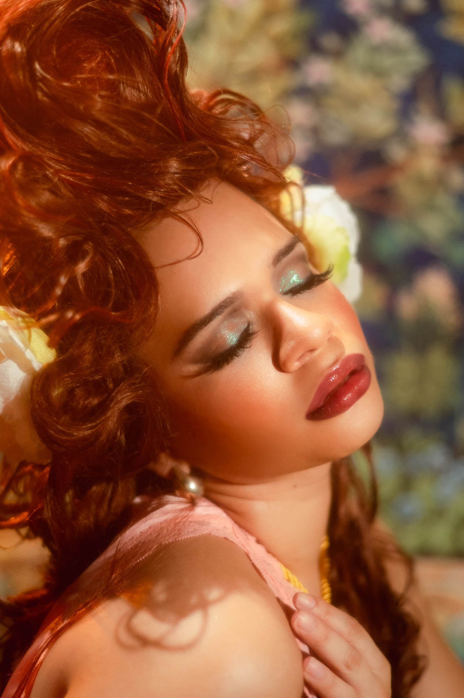 Close up profile of a woman with closed eyes and shimmering teal eyeshadow, her curling wig and peony softly blurred behind her, Royal Lune Photo.